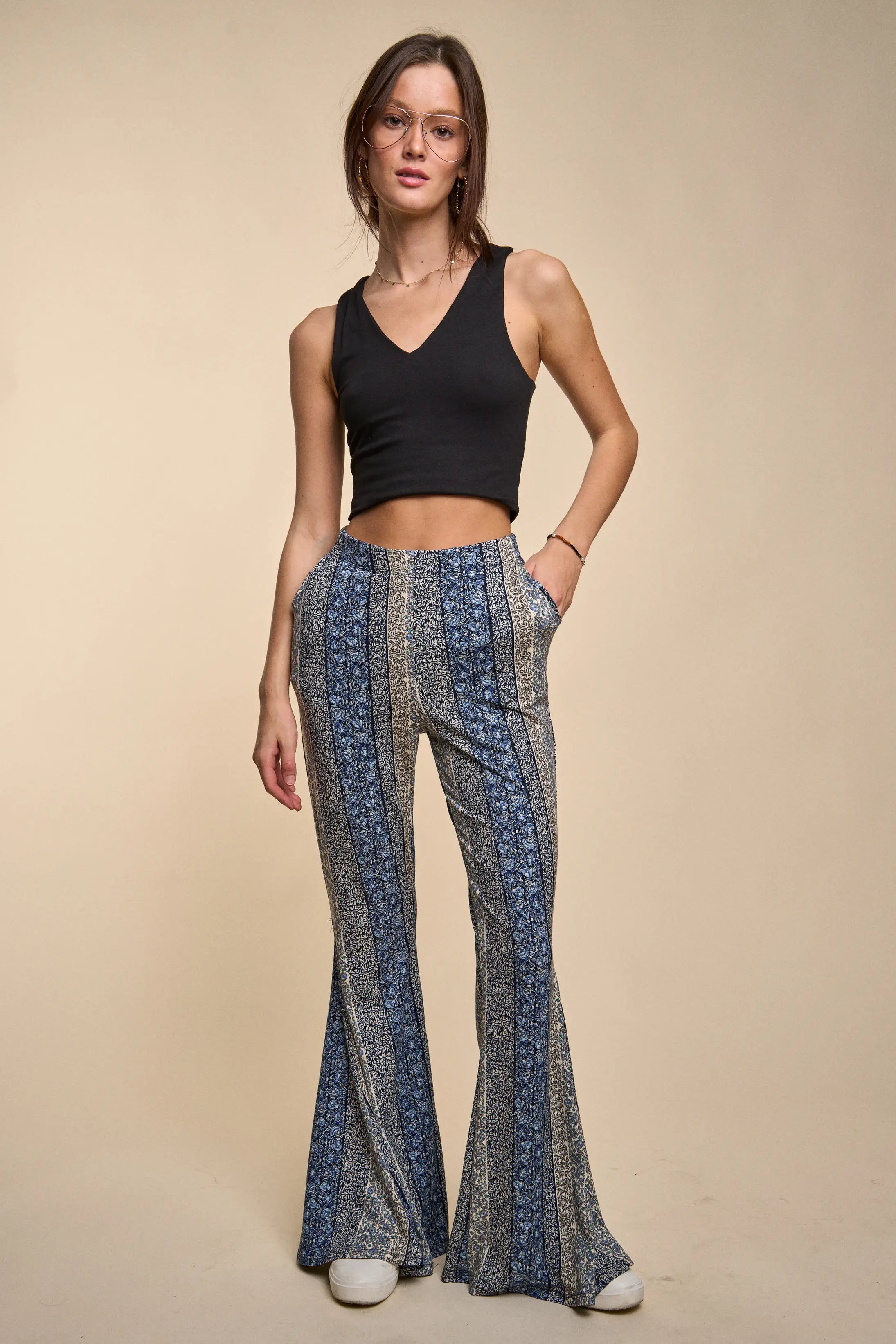 Fleetwood Floral Bell Bottoms in navy with vertical mixed floral and geometric stripes, worn with a black sleeveless crop top and white sneakers on a beige background