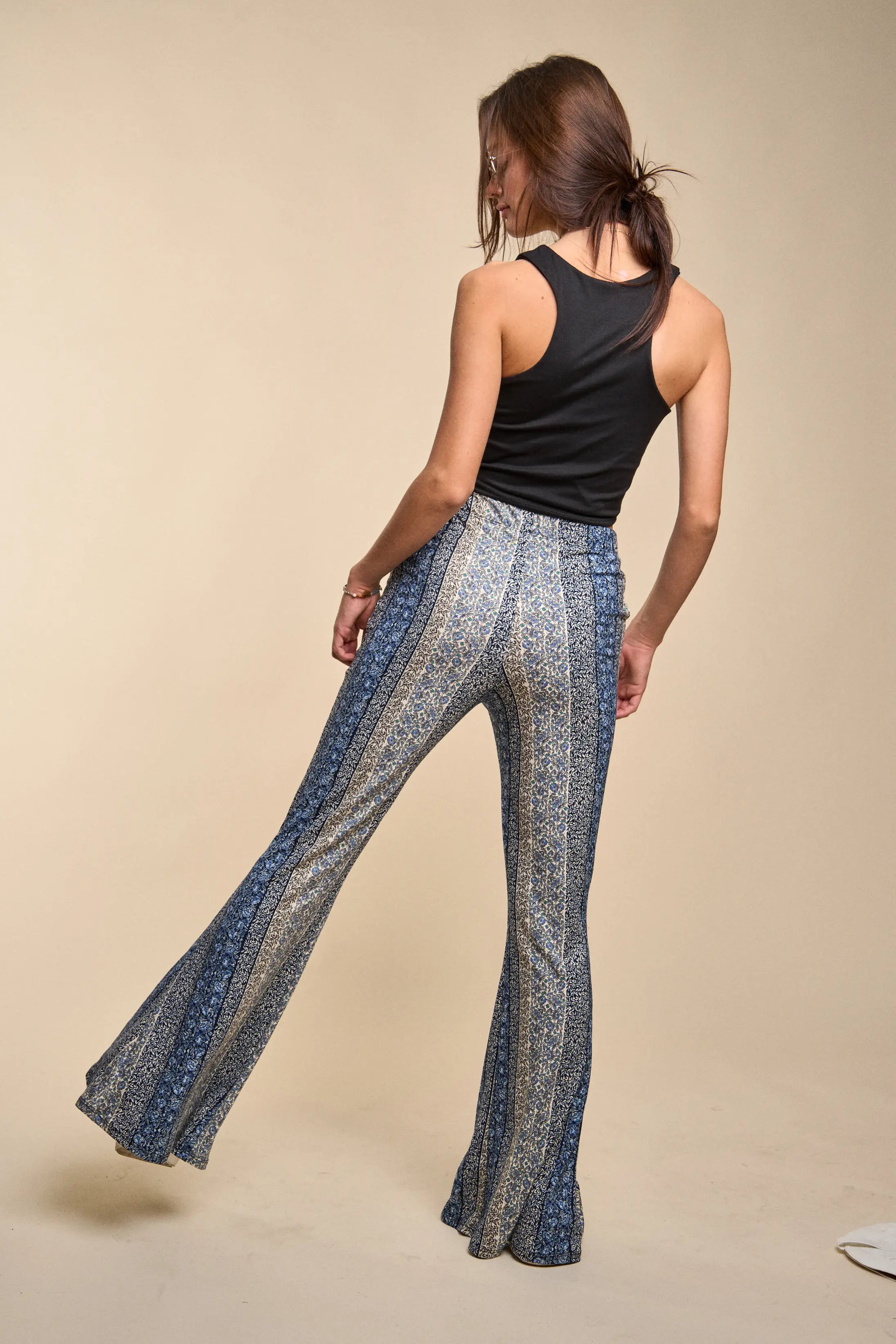 Fleetwood Floral Bell Bottoms in navy with vertical intricate floral patterns worn with a black sleeveless top on a neutral beige background