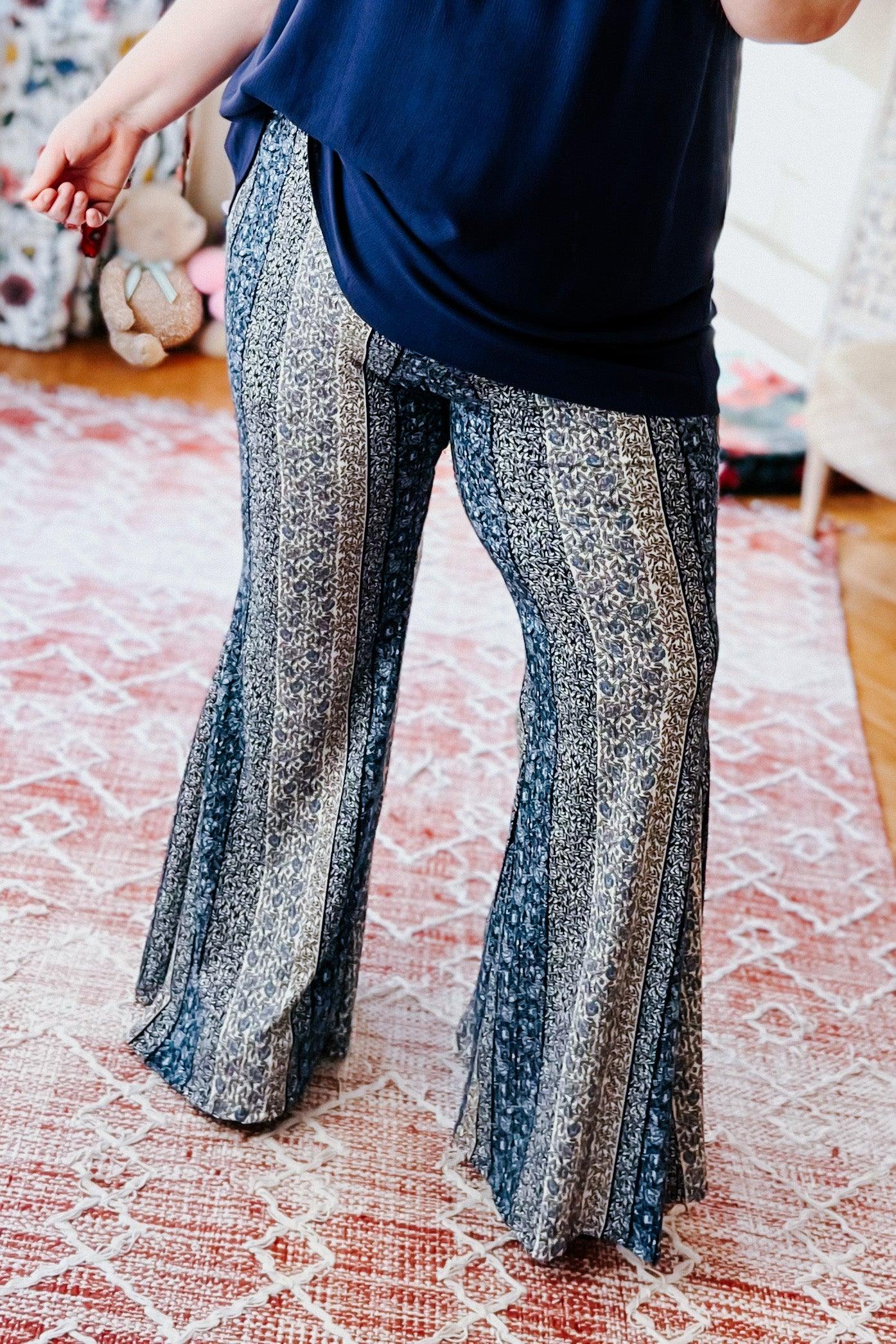 Fleetwood Floral Bell Bottoms in navy with vertical intricate lace-inspired stripes, worn with a loose navy top on a soft textured rug in a casual home setting