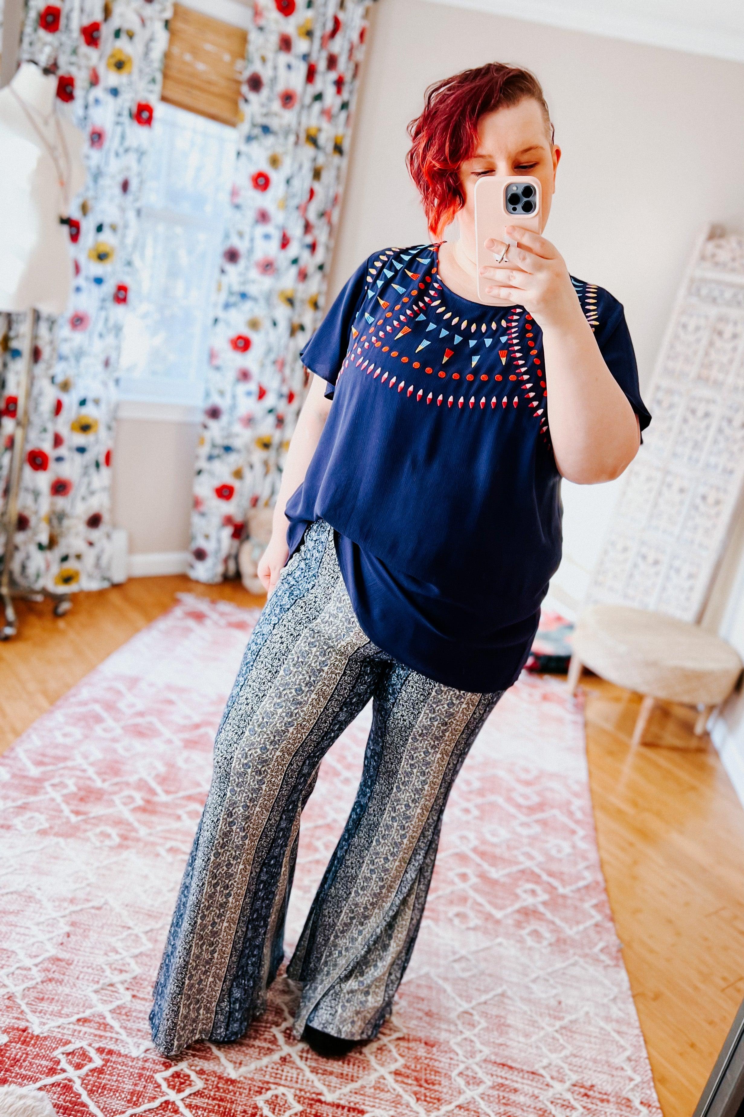 Fleetwood Floral Bell Bottoms in navy with vertical paisley and floral-inspired stripes, paired with a navy patterned top in a cozy bright room setting.