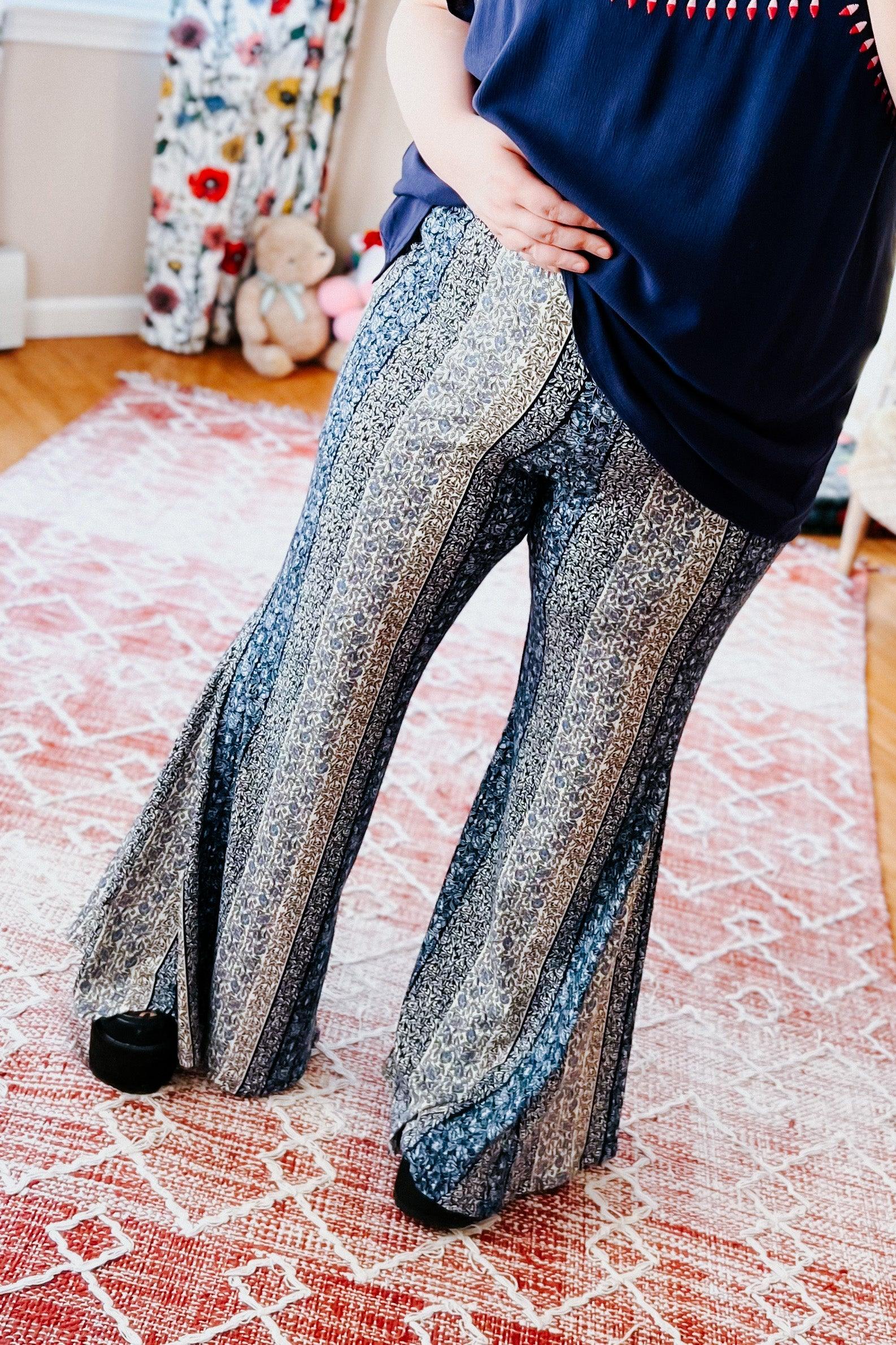 Fleetwood Floral Bell Bottoms in navy with vertical striped floral and abstract patterns, styled with a navy top and black shoes on a patterned rug indoors.
