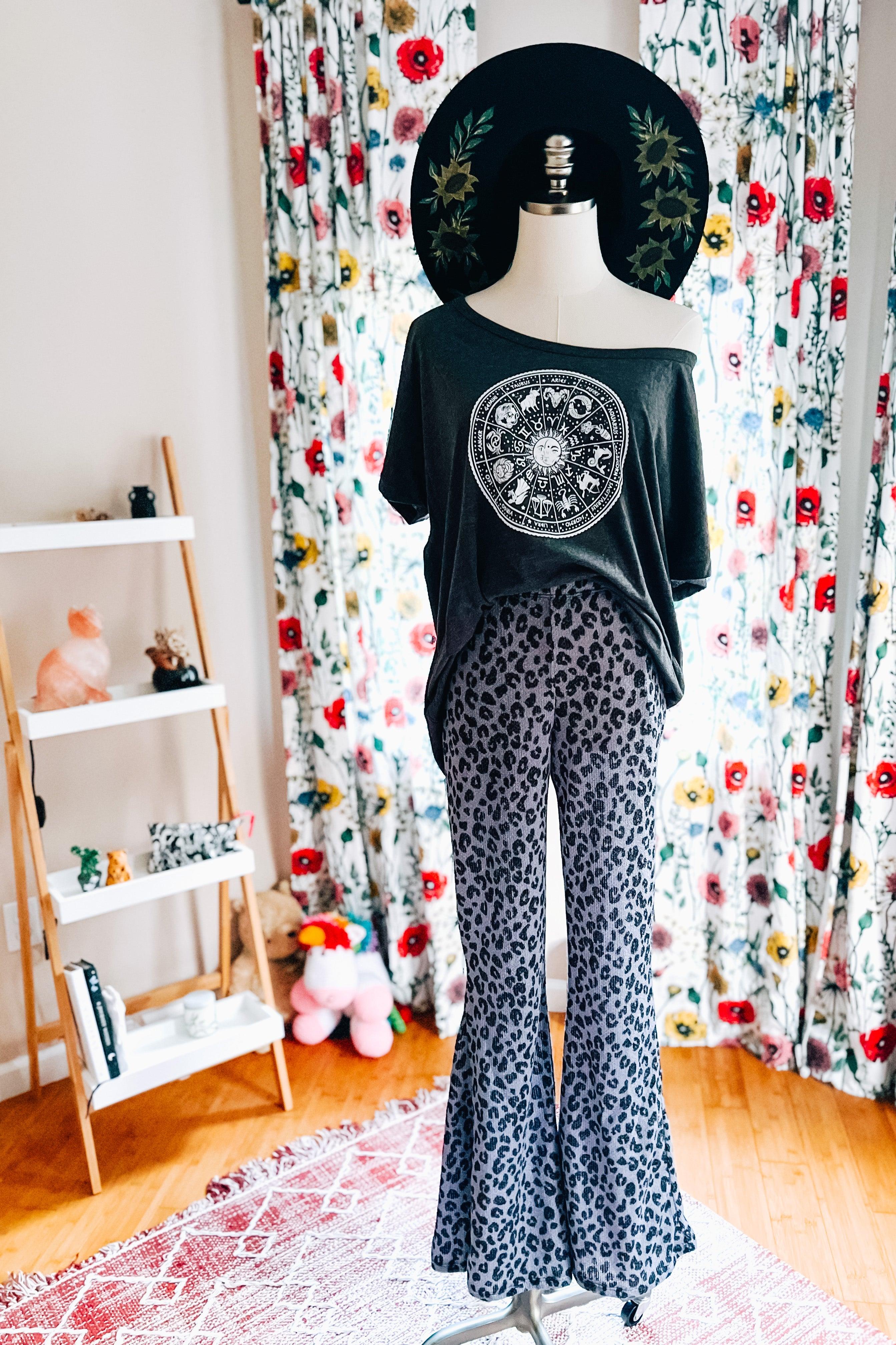 Mannequin dressed in dark graphic off-shoulder top with blue wide-legged leopard print pants and black floral hat indoors