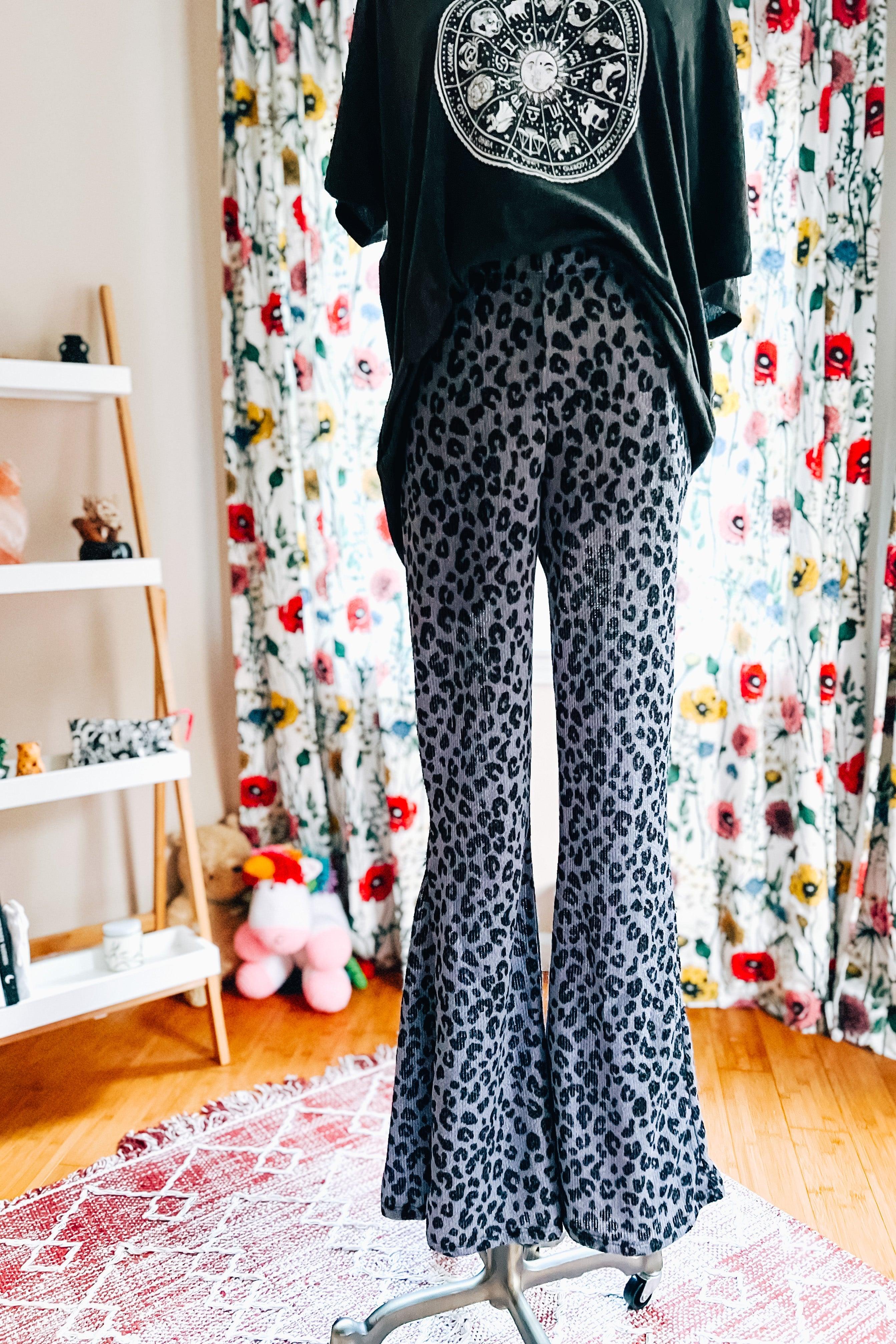 Blue leopard print flared pants displayed on mannequin in colorful room with floral curtains and hardwood floor