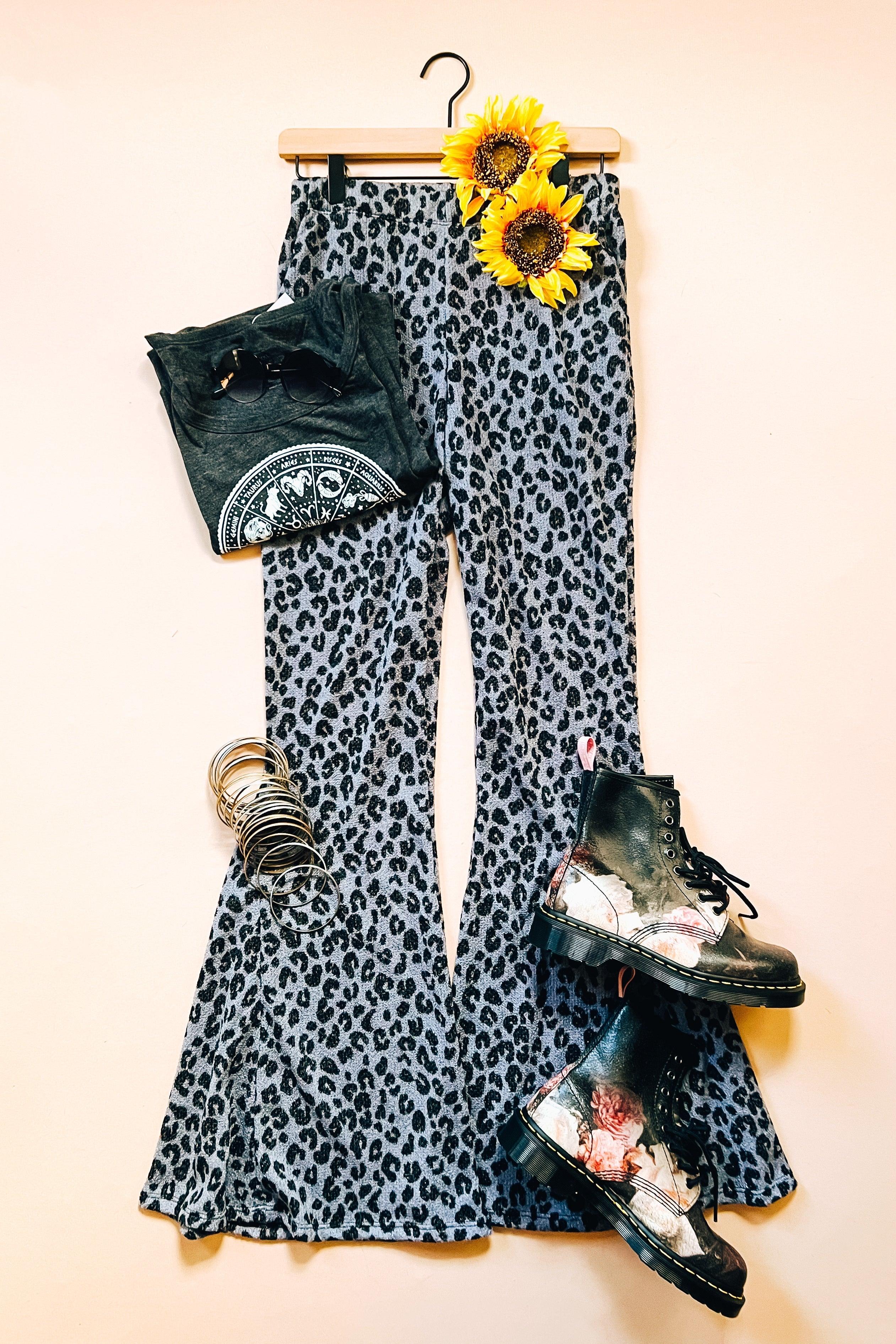 Blue leopard print flared pants styled with black graphic tee, silver bangles, sunflower accents, and floral black combat boots laid flat