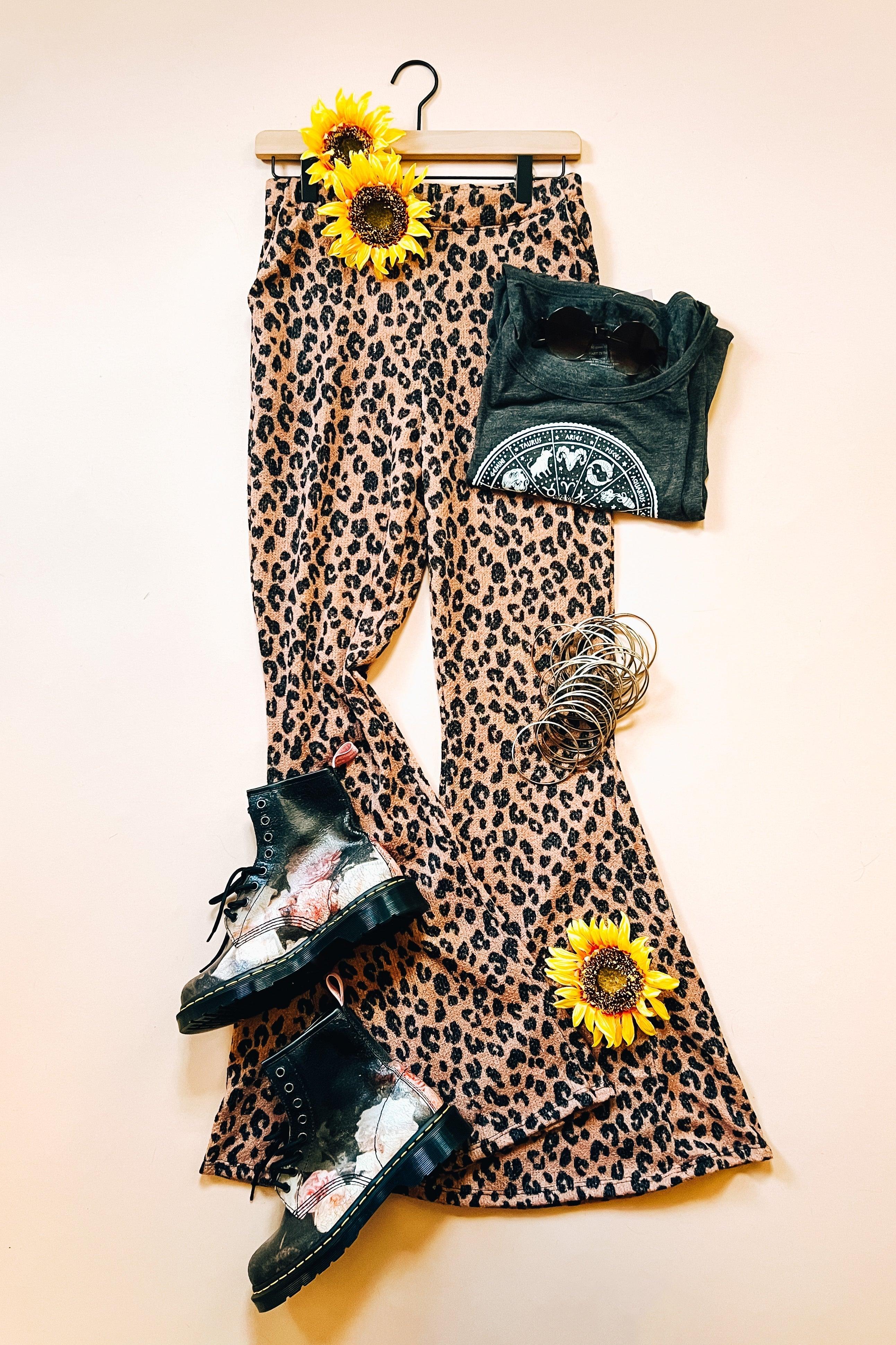 Mocha leopard print bell bottoms styled with graphic tee, black floral boots, silver bracelets, sunglasses, and yellow sunflowers on hanger