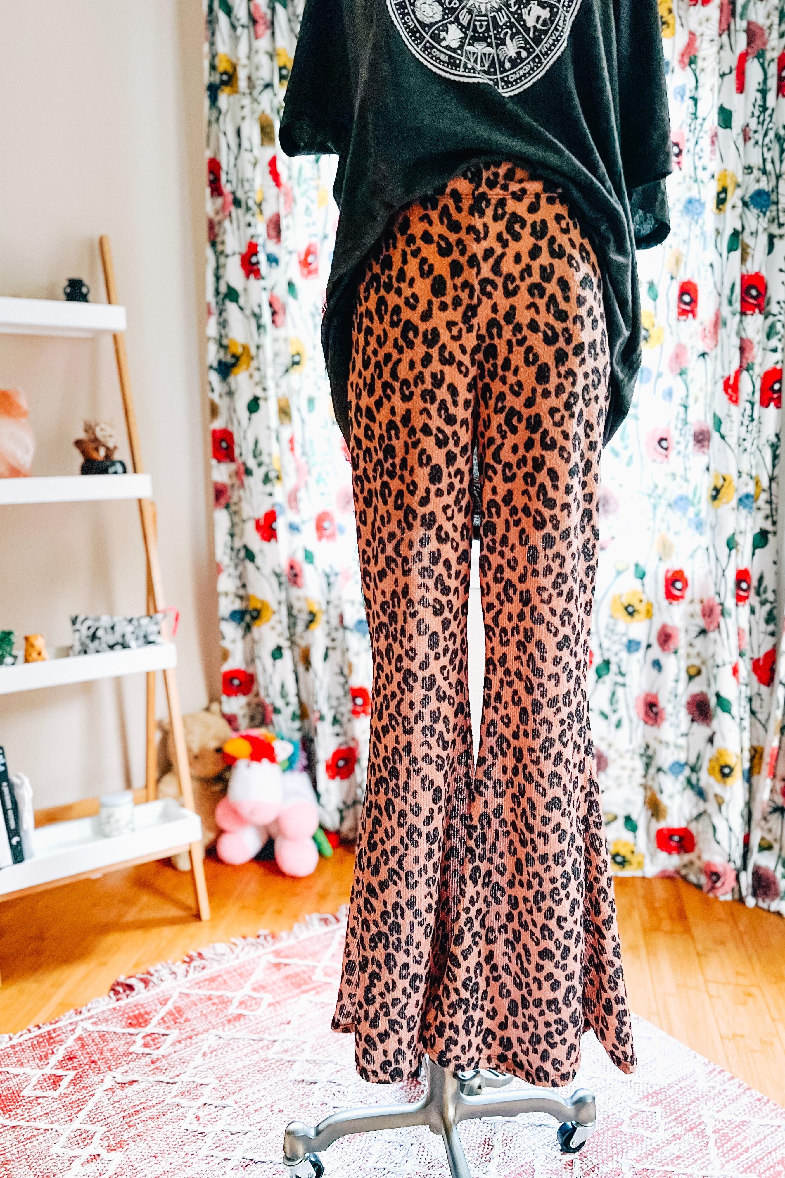 Mocha leopard print bell bottoms displayed on dress form with loose black graphic top and floral curtain background