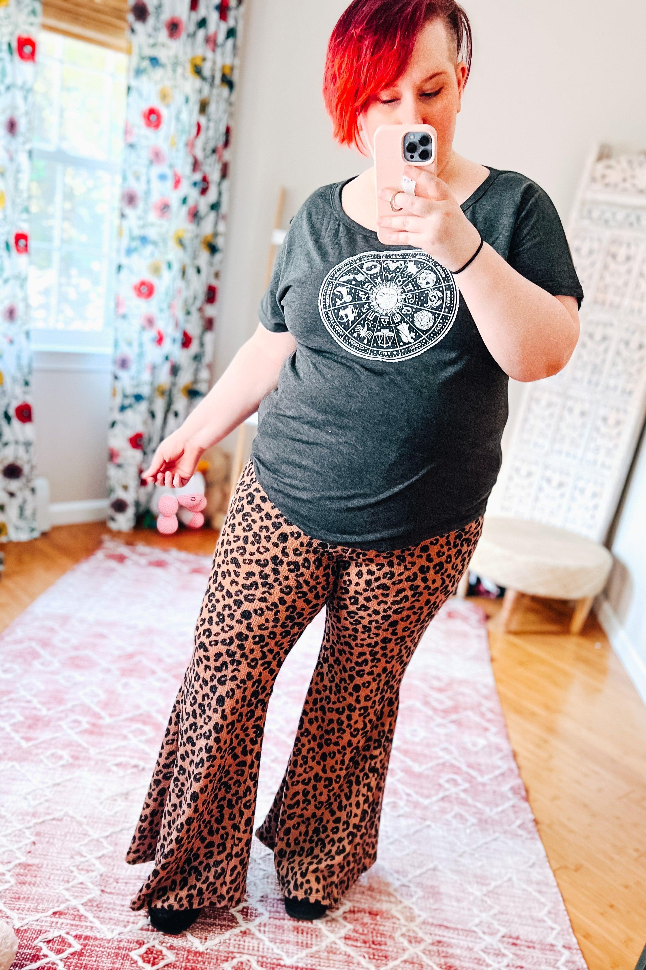 Woman taking selfie wearing mocha leopard print flared bell bottoms with black astrology graphic t-shirt in bright room