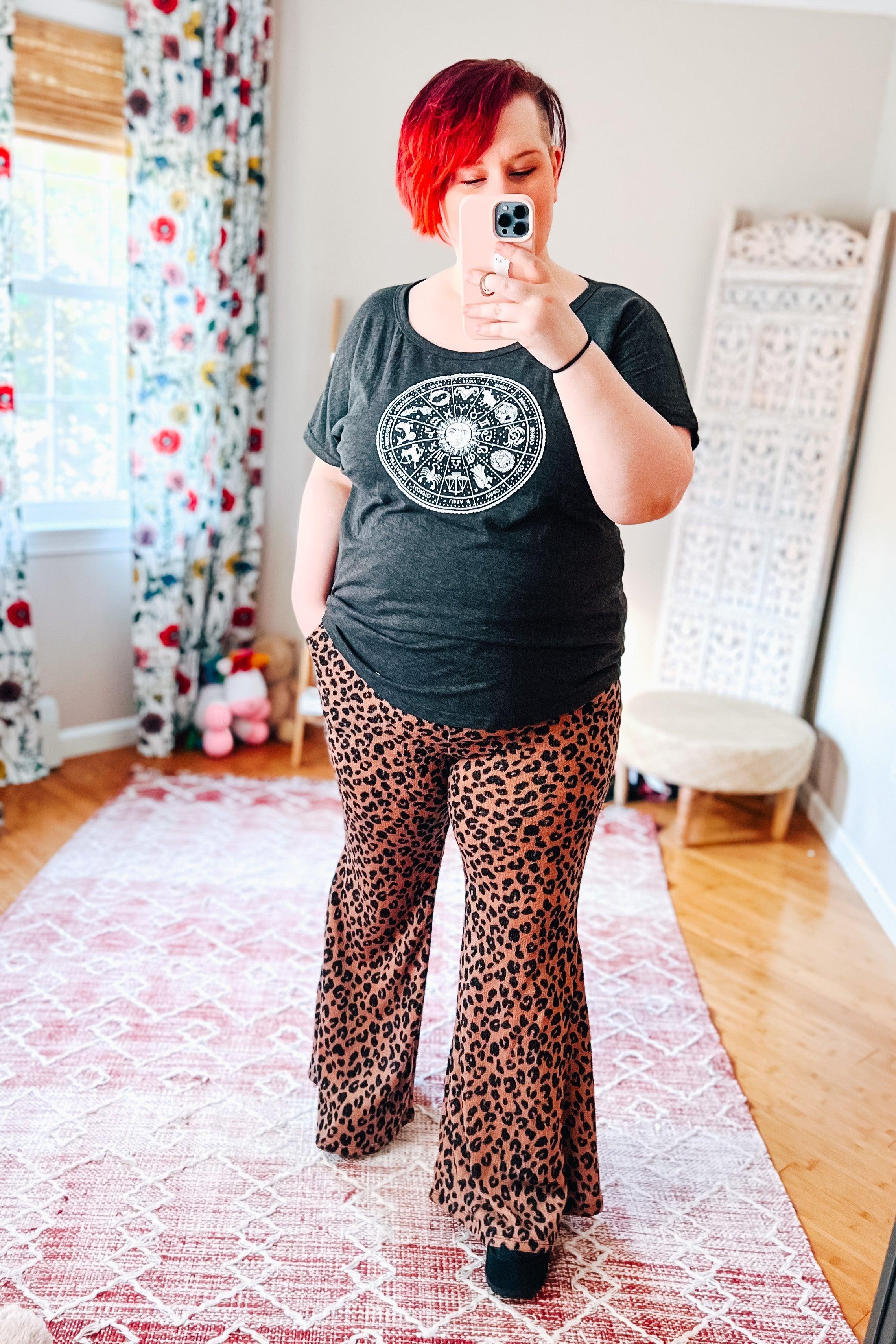Woman taking mirror selfie wearing mocha leopard print bell bottoms with black graphic t-shirt in bright room