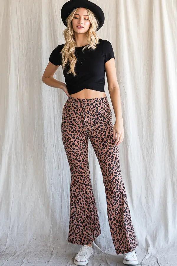 Woman wearing mocha leopard print high-waisted bell bottoms with black cropped t-shirt and black hat against pale backdrop