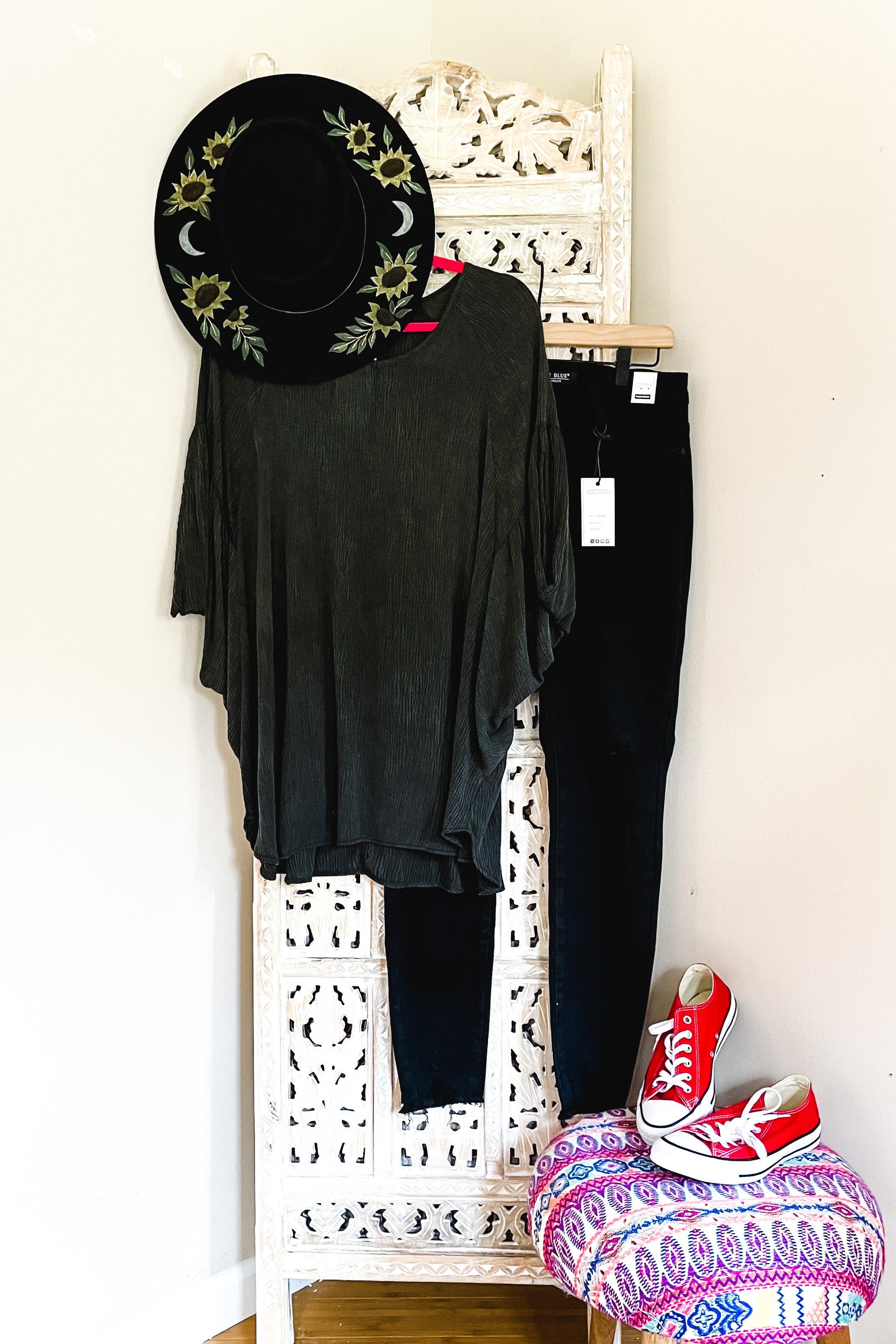Charcoal oversized tunic with flowy sleeves paired with black pants, embroidered black hat, and red canvas sneakers styled on divider