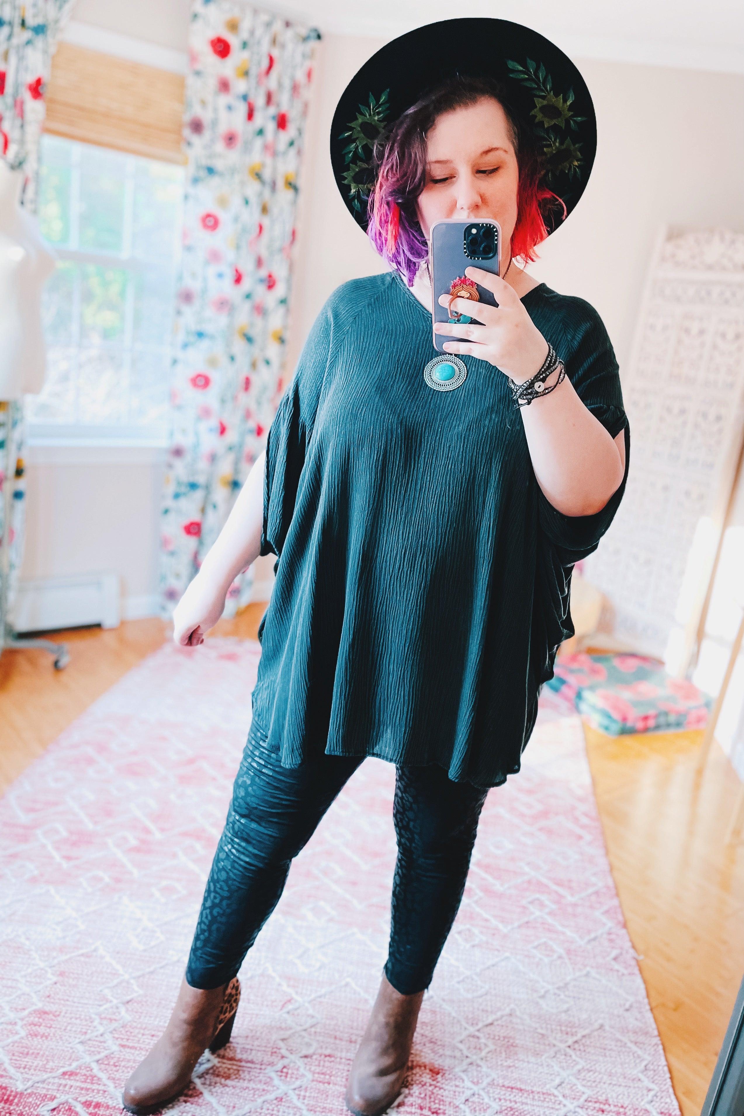 Woman wearing charcoal loose tunic with flowing sleeves and textured black leggings taking mirror selfie indoors