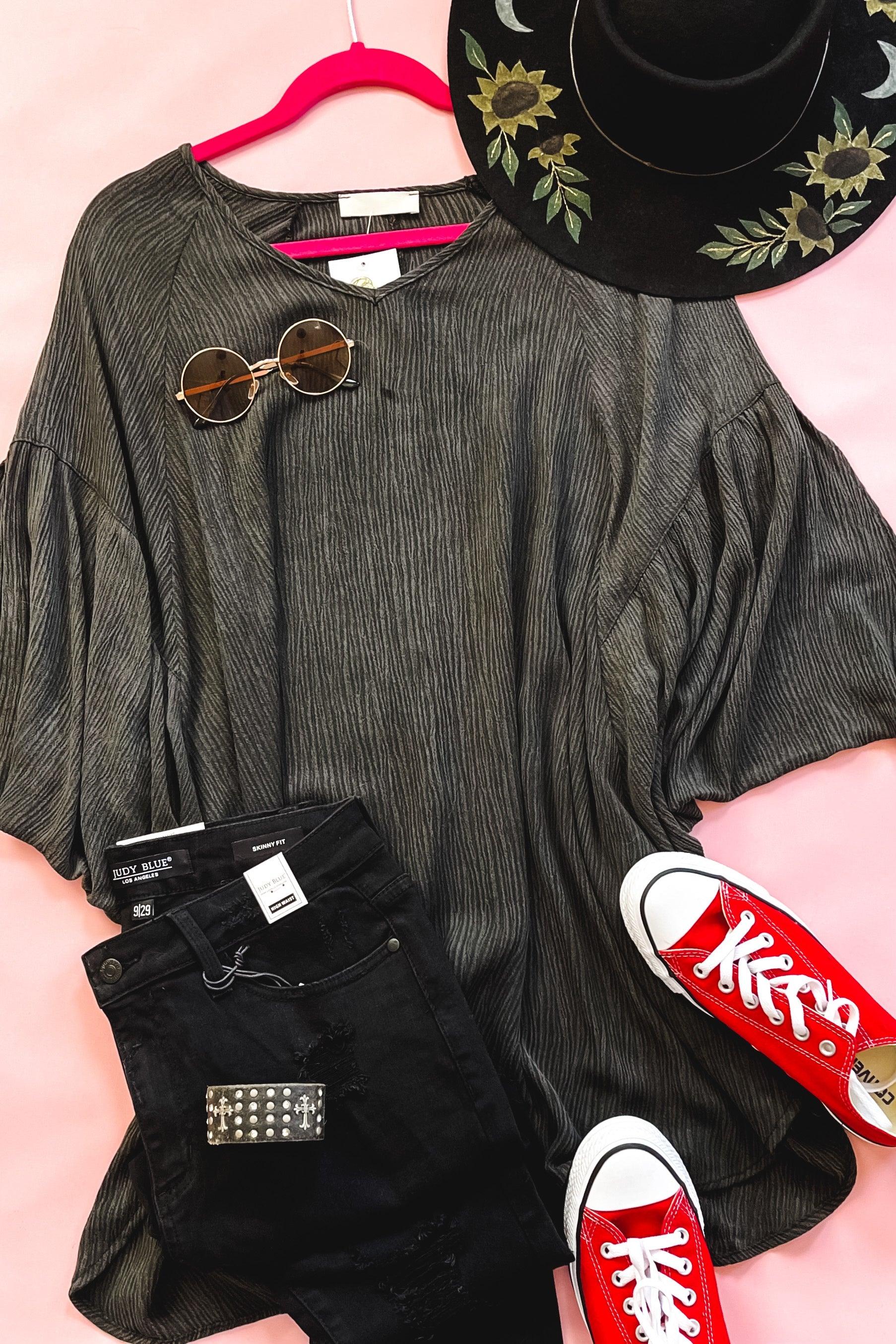 Charcoal loose tunic with subtle pinstripes styled with black jeans, round sunglasses, embroidered black hat, and red canvas shoes on pink background