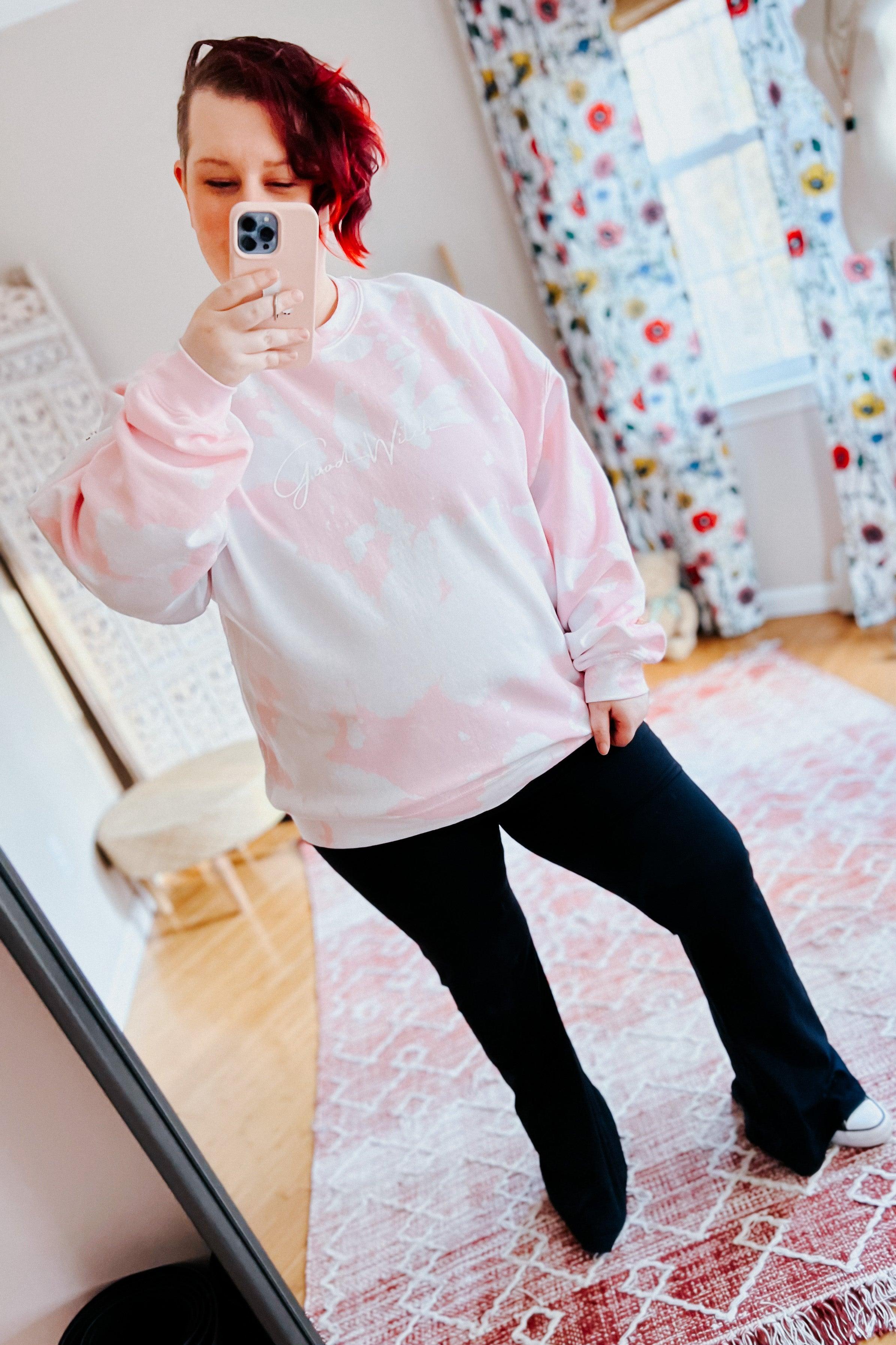 Woman posing in home wearing pastel pink bleached pullover with white script paired with black pants on patterned rug