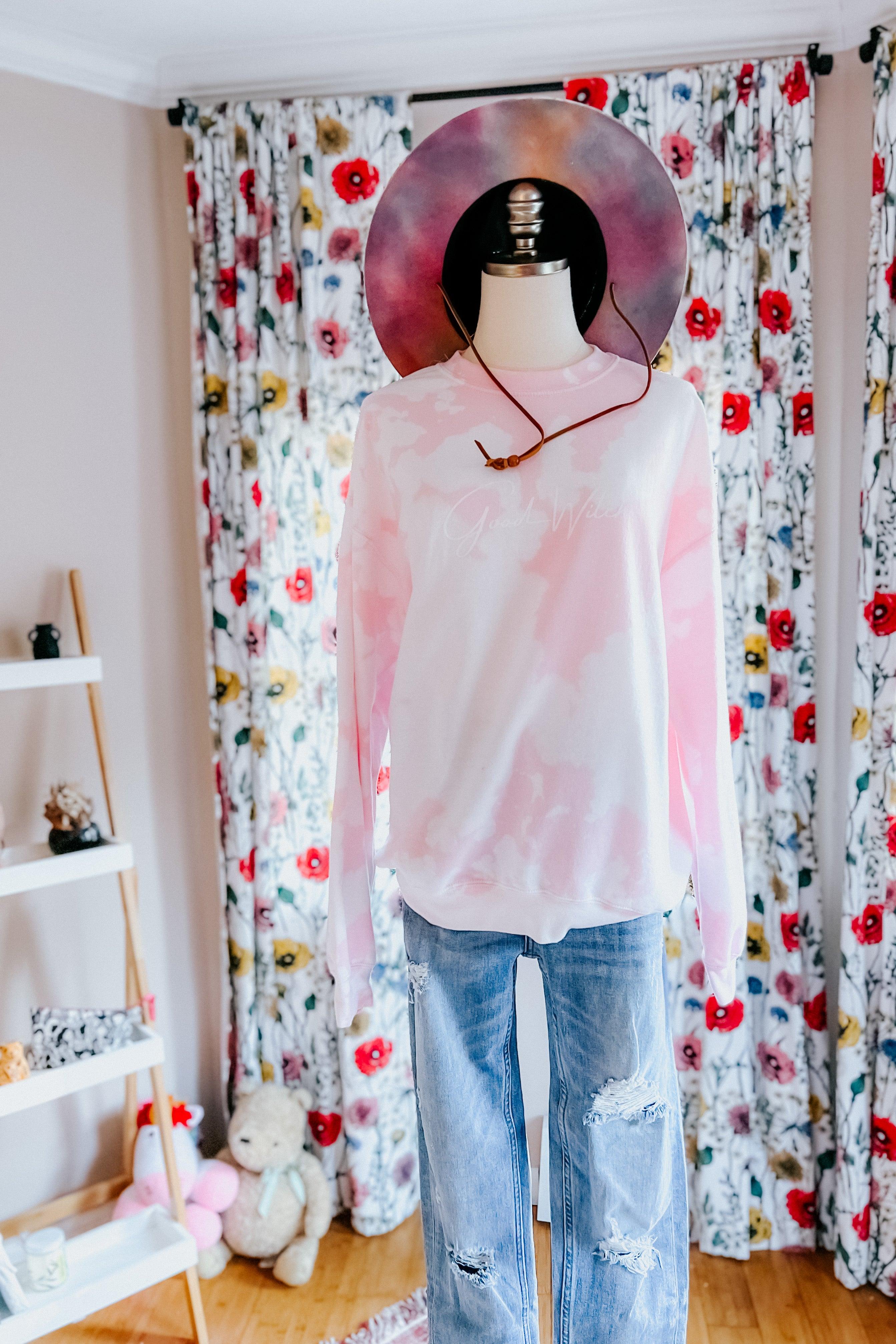 Mannequin wearing pastel pink and white bleached pullover paired with distressed blue jeans and wide-brimmed hat indoors
