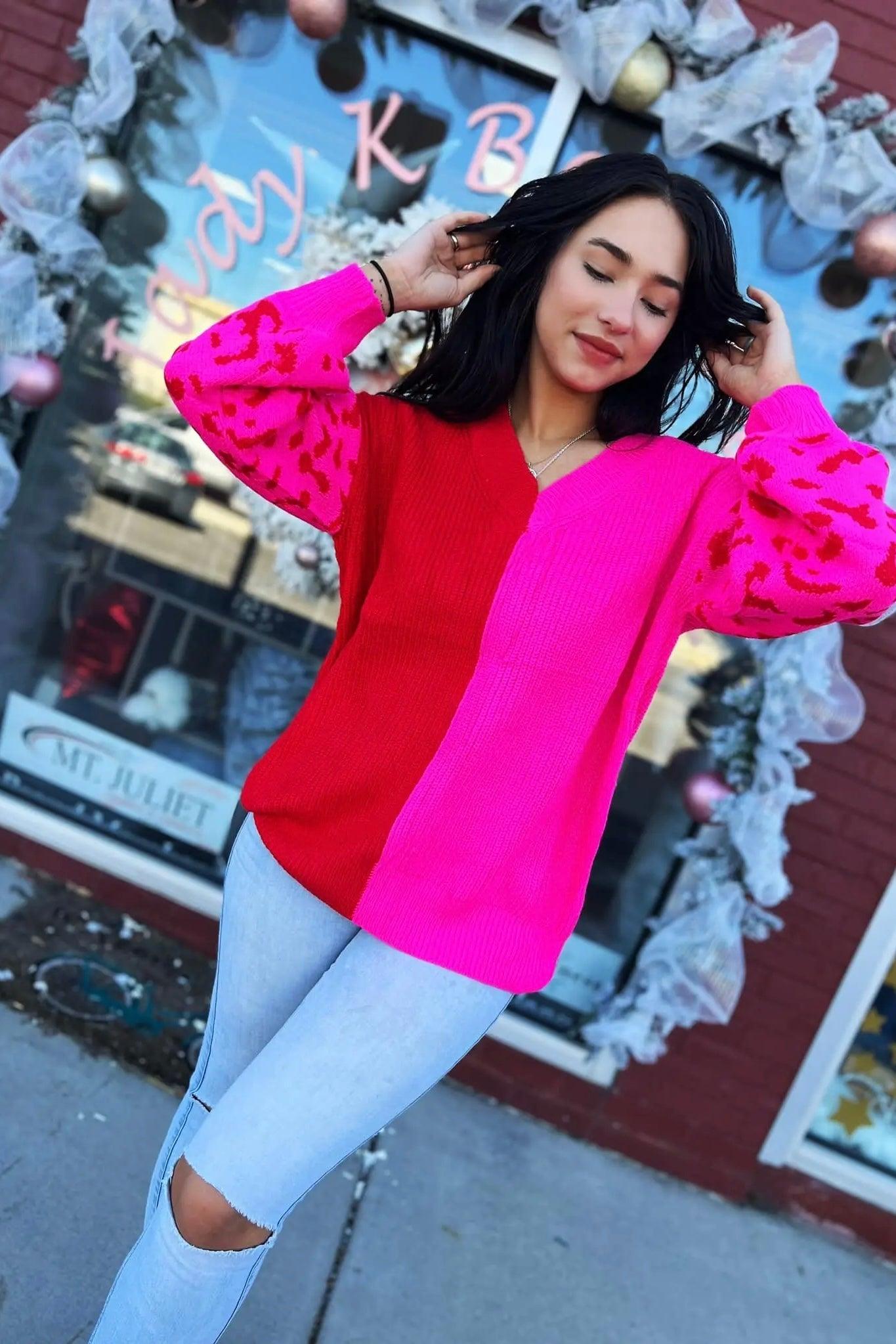Woman wearing bold pink and red color block sweater with leopard print sleeves paired with ripped light jeans outdoors