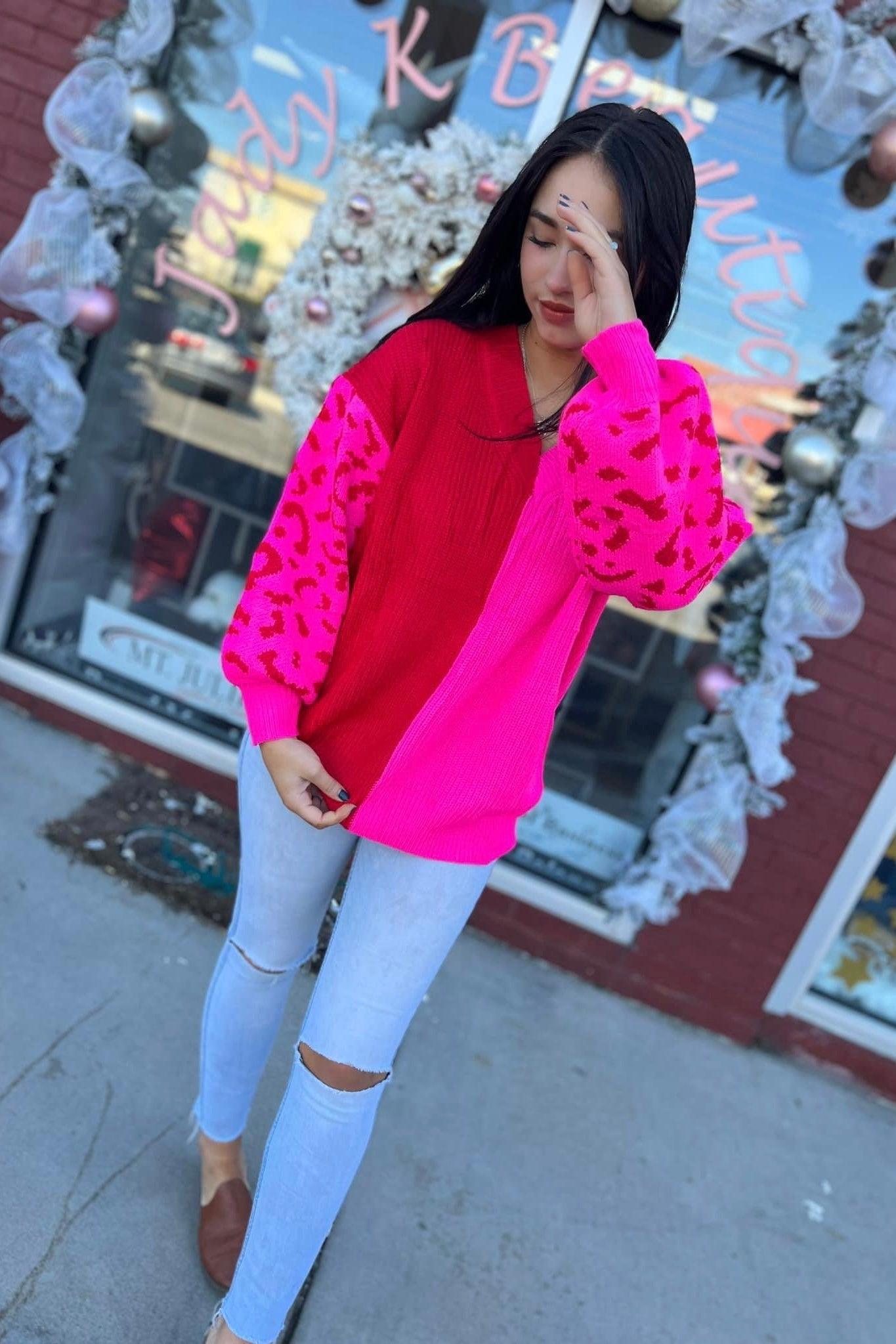 Woman wearing bright pink and red color block sweater with leopard print sleeves and ripped light jeans outdoors