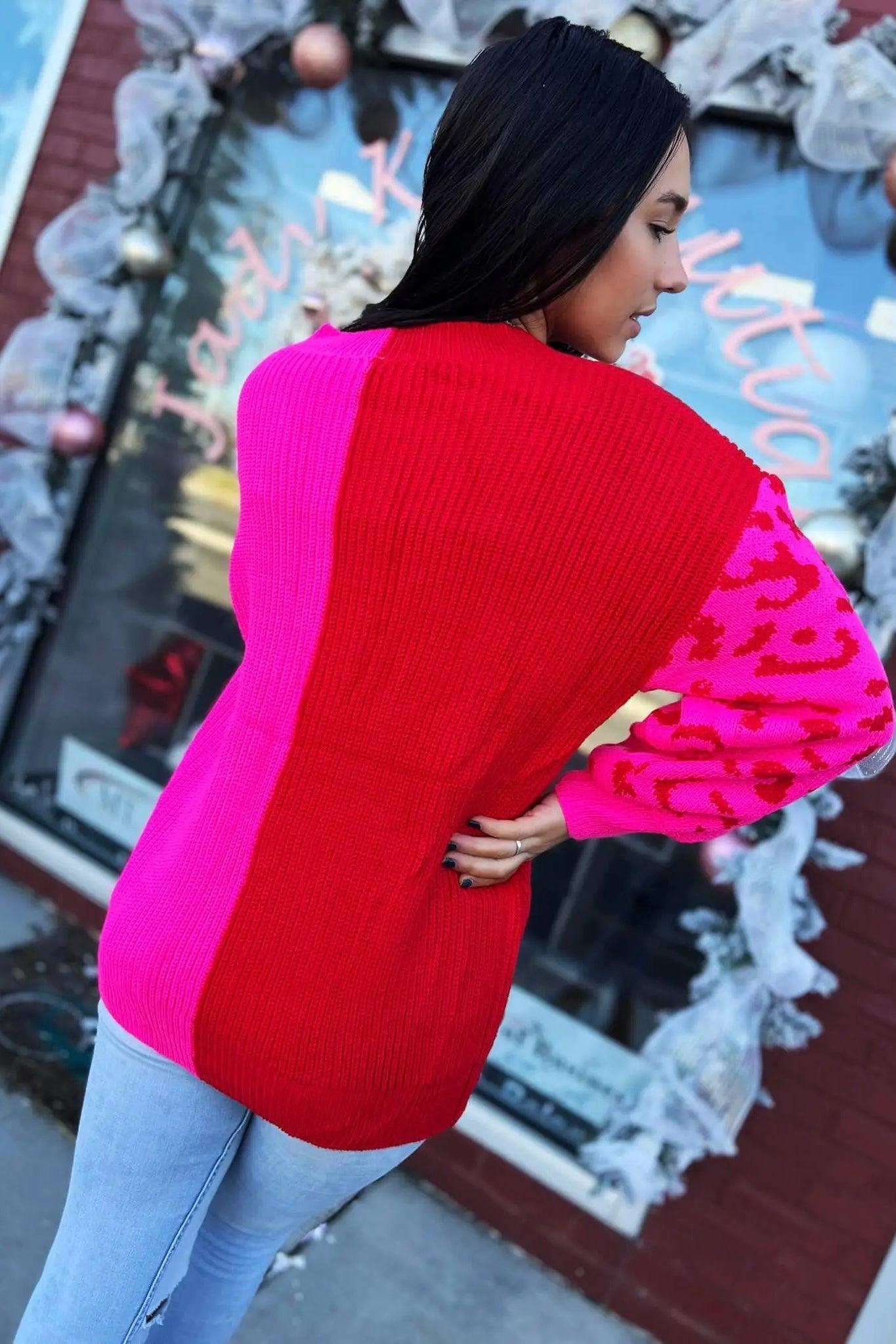 Woman wearing vibrant pink and red color block sweater with leopard print sleeve paired with light washed jeans outdoors
