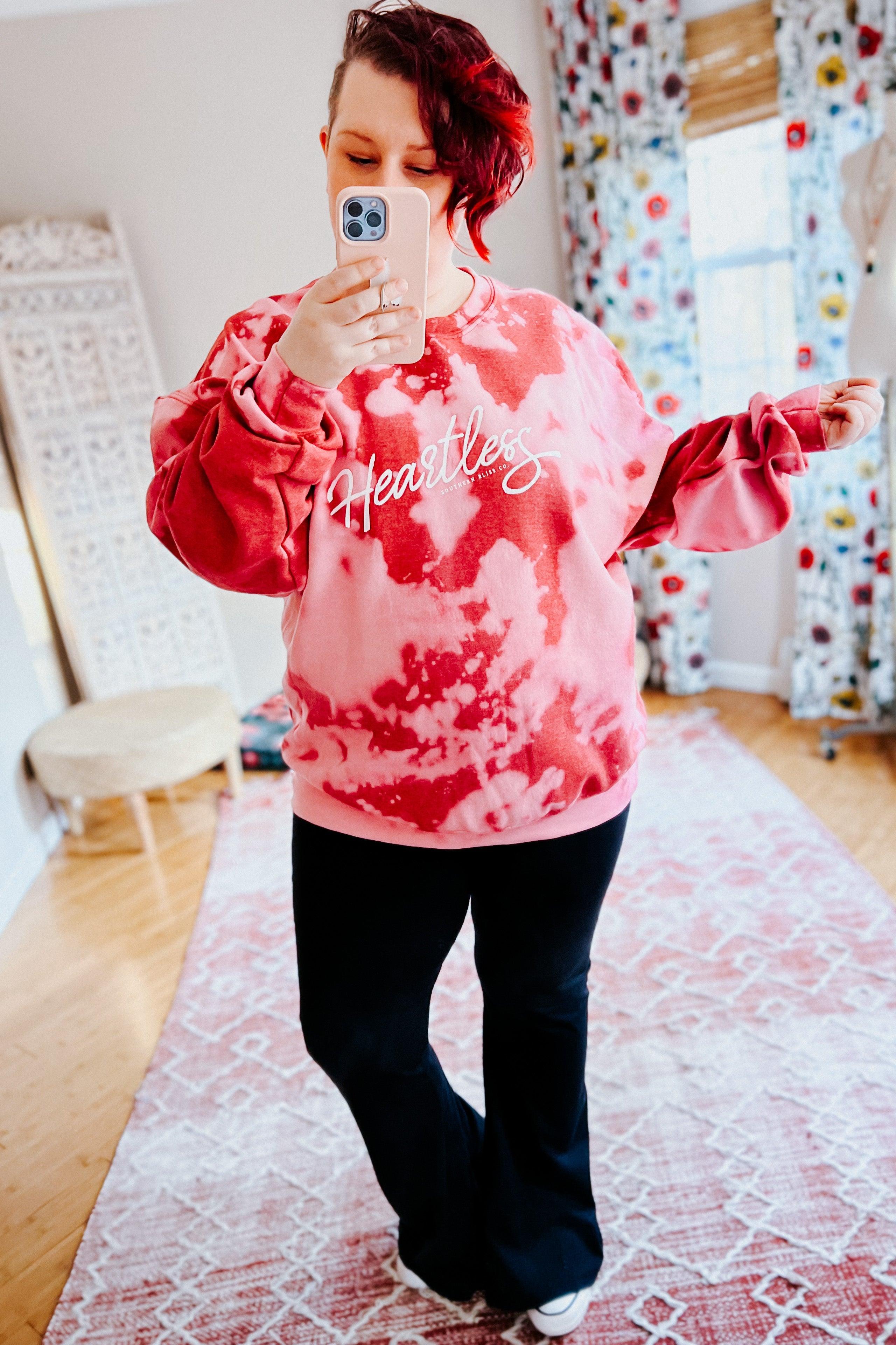 Woman taking indoor selfie wearing red heartless bleached pullover with white script logo and black pants