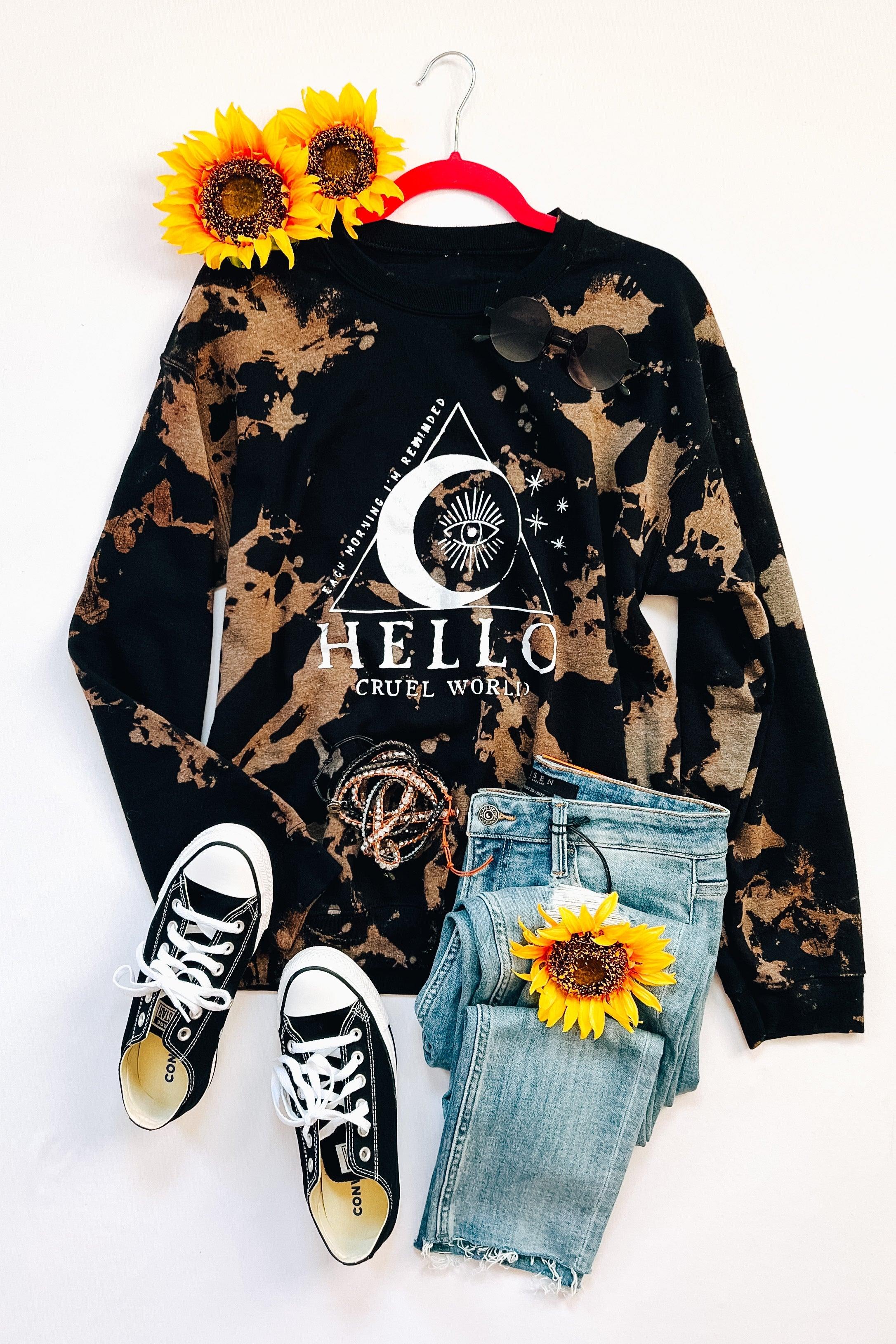 Black bleached sweatshirt with celestial eye design paired with light wash jeans, black sneakers, sunglasses, and sunflowers on white background
