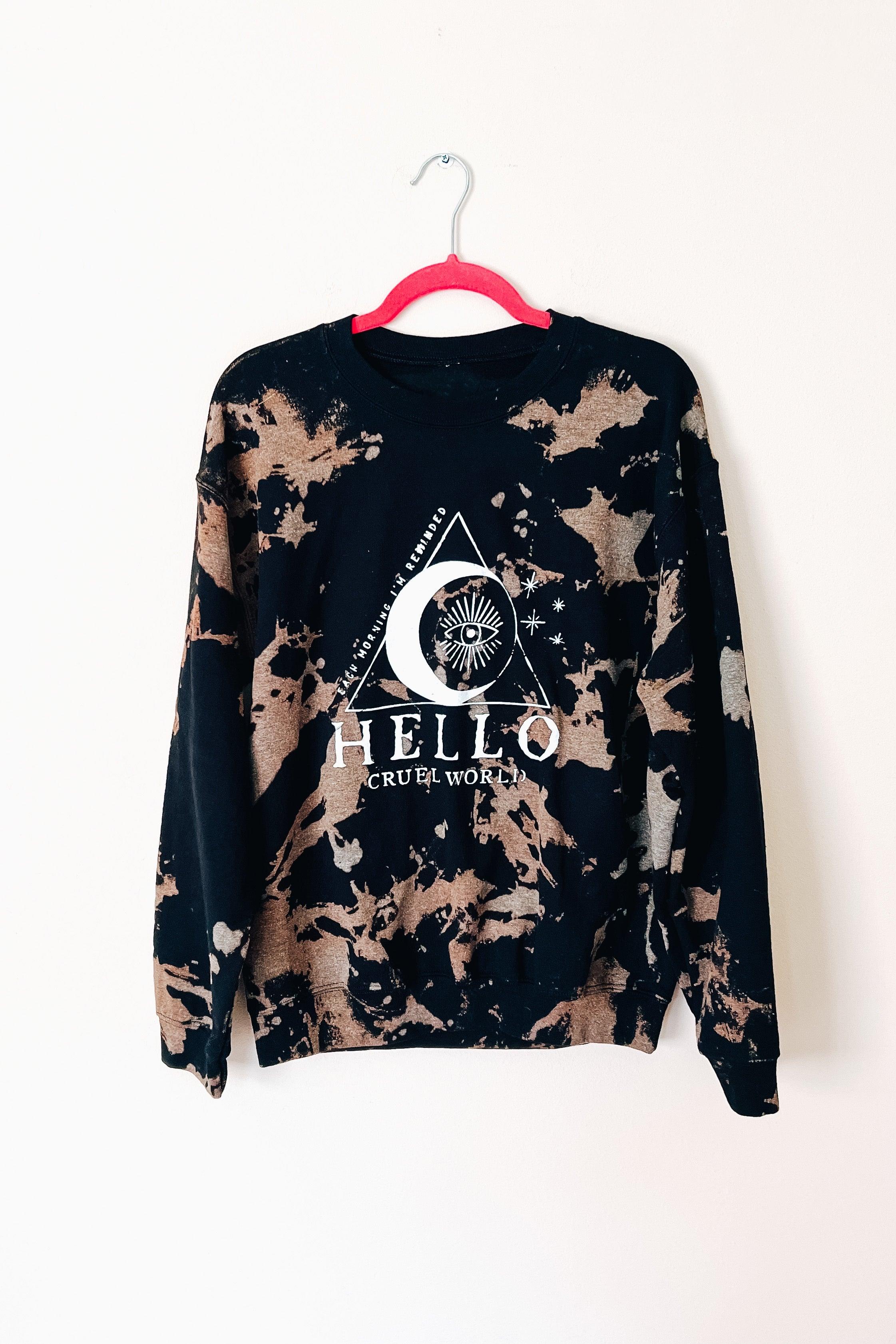 Black sweatshirt with bleached splatter pattern and celestial eye graphic centered on front hanging on pink hanger against white wall