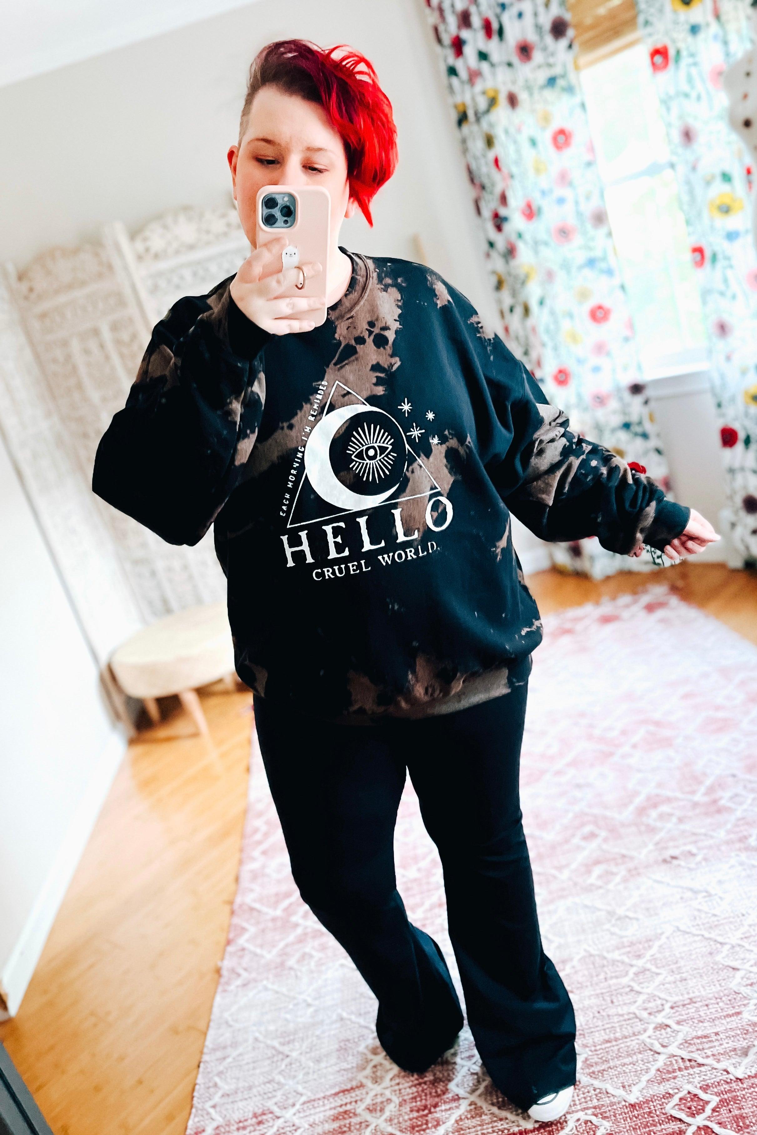 Woman with red hair taking selfie wearing black Hello Cruel World bleached sweatshirt with celestial print in bright room