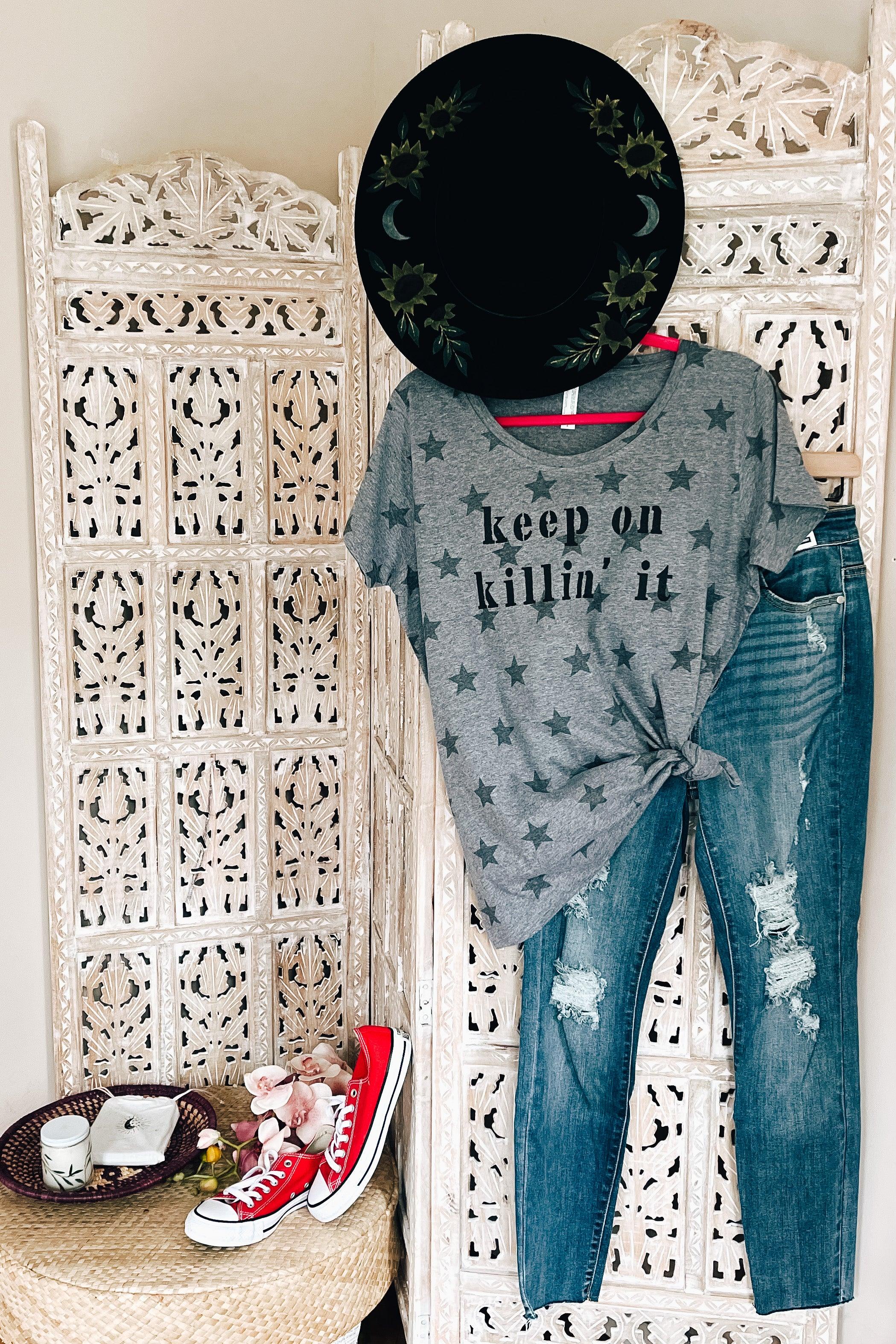Grey Keep On Killin’ It Star Tee with black star pattern styled with ripped blue jeans and black hat on carved wooden room divider