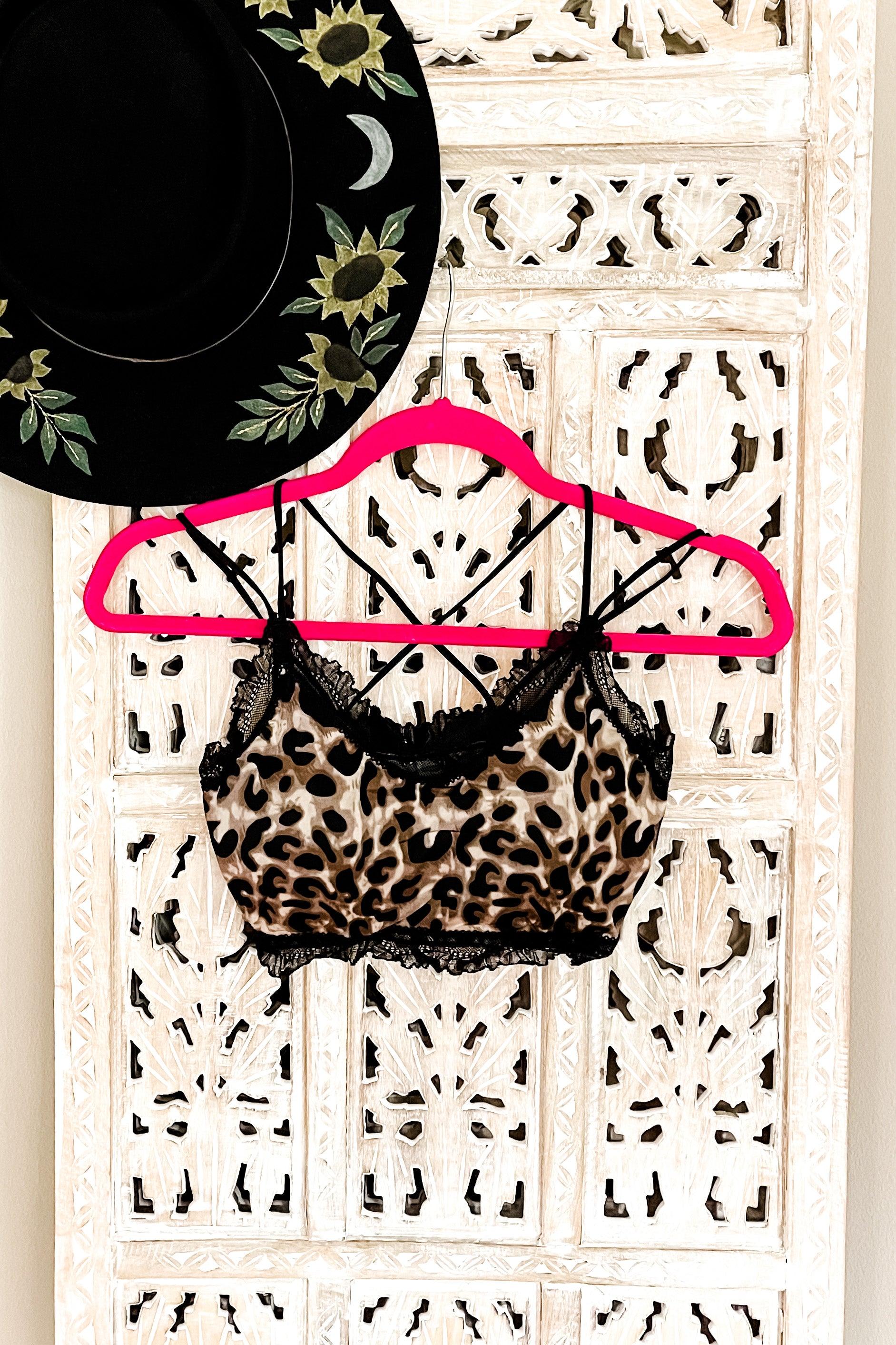 Brown and black leopard print bralette with black lace trim hanging on pink hanger against carved white wood panel