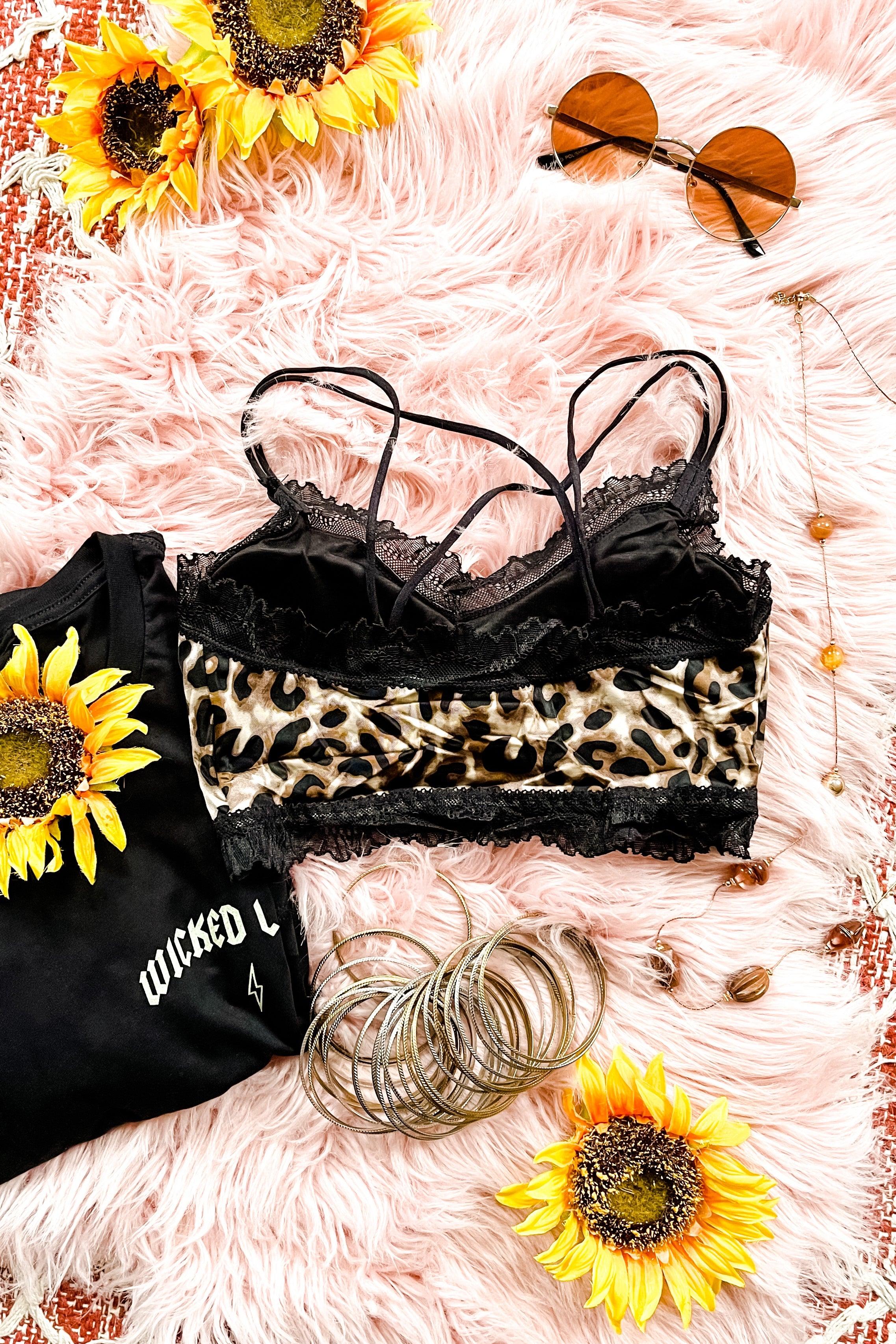 Leopard print bralette with black lace trim and thin crisscross straps styled with sunglasses and silver bangles on pink fur