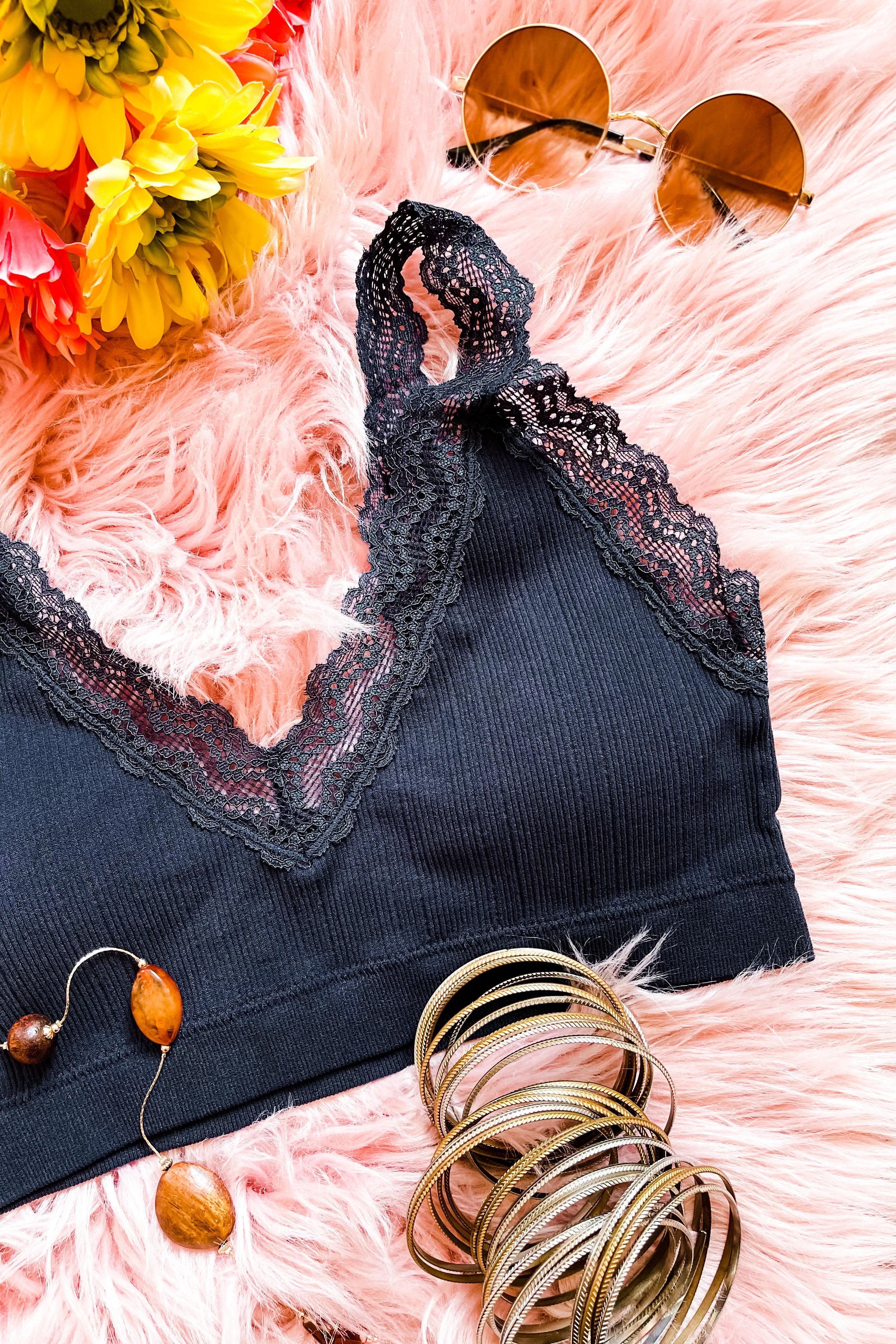 Navy ribbed bralette with lace trim on soft pink fur surface with gold bangles, amber earrings, round sunglasses, and yellow flowers nearby