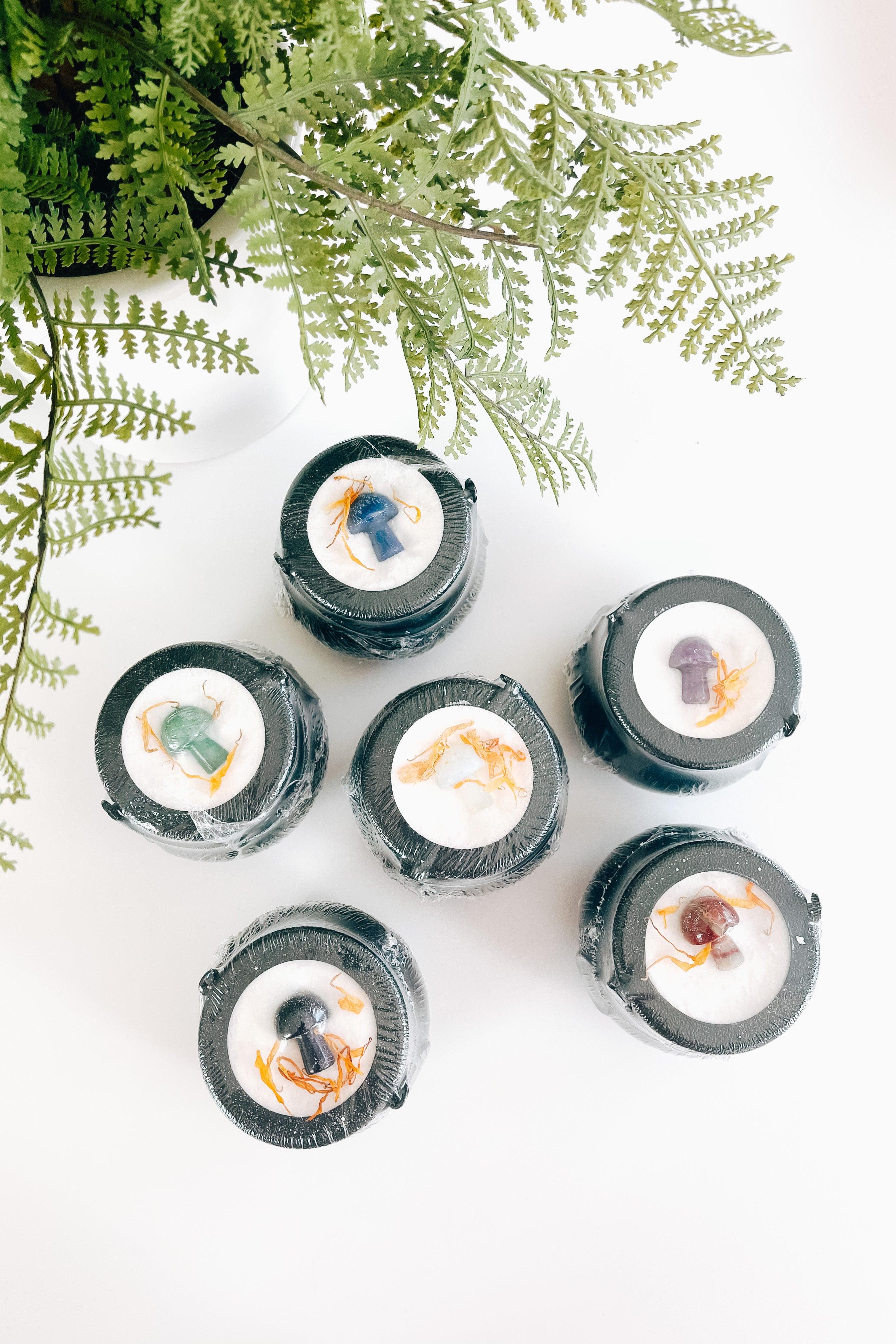 Set of six black cauldron bath bombs featuring colorful mushroom shapes and dried flower accents on white surface