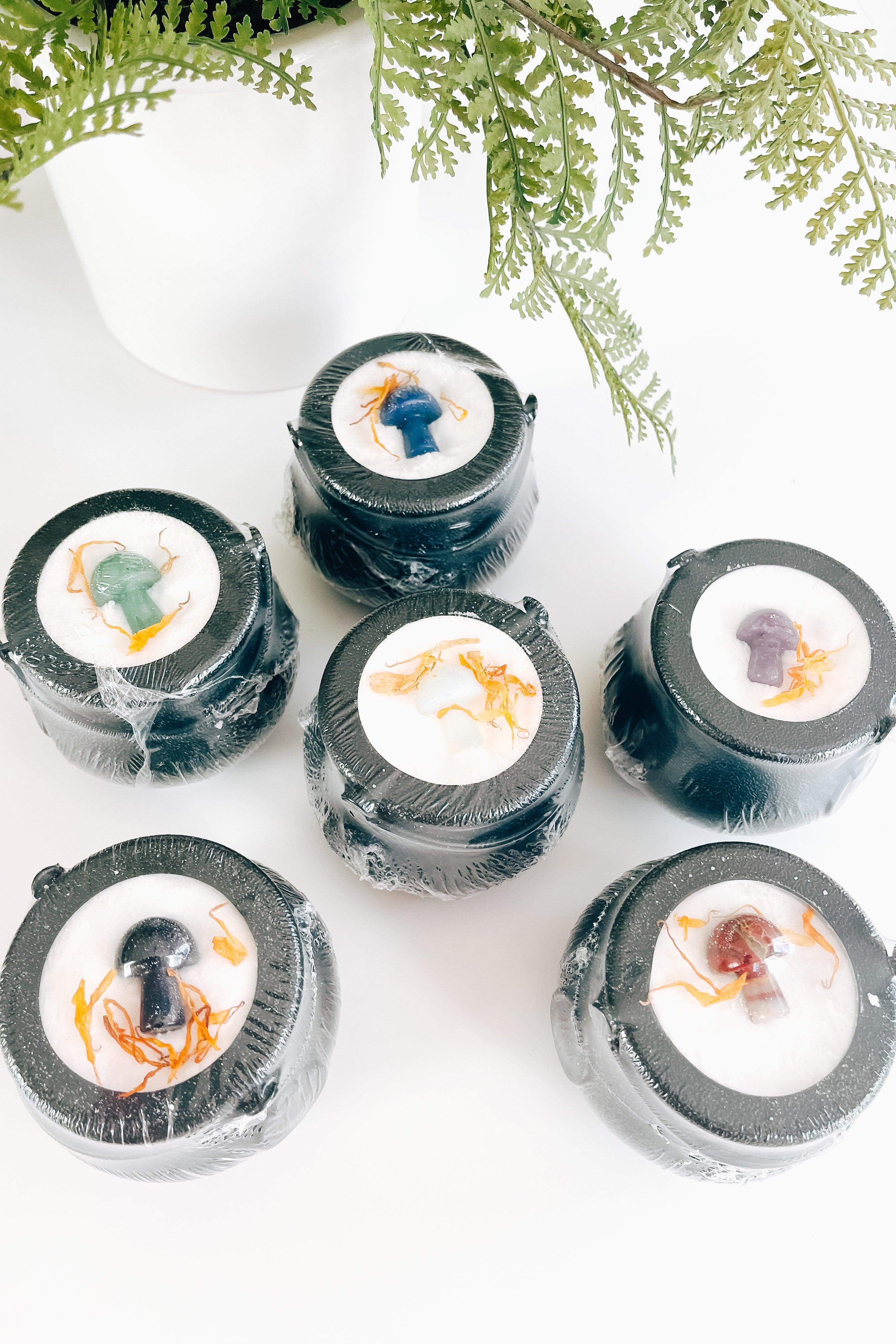 Set of six black cauldron bath bombs featuring colorful mushroom shapes and orange dried flower accents on white surface