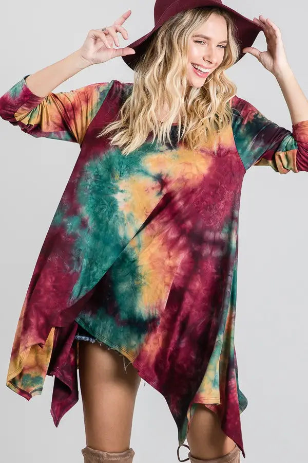 Asymmetrical ruby tie-dye top with green and yellow accents, styled with a wide-brim hat and knee-high boots