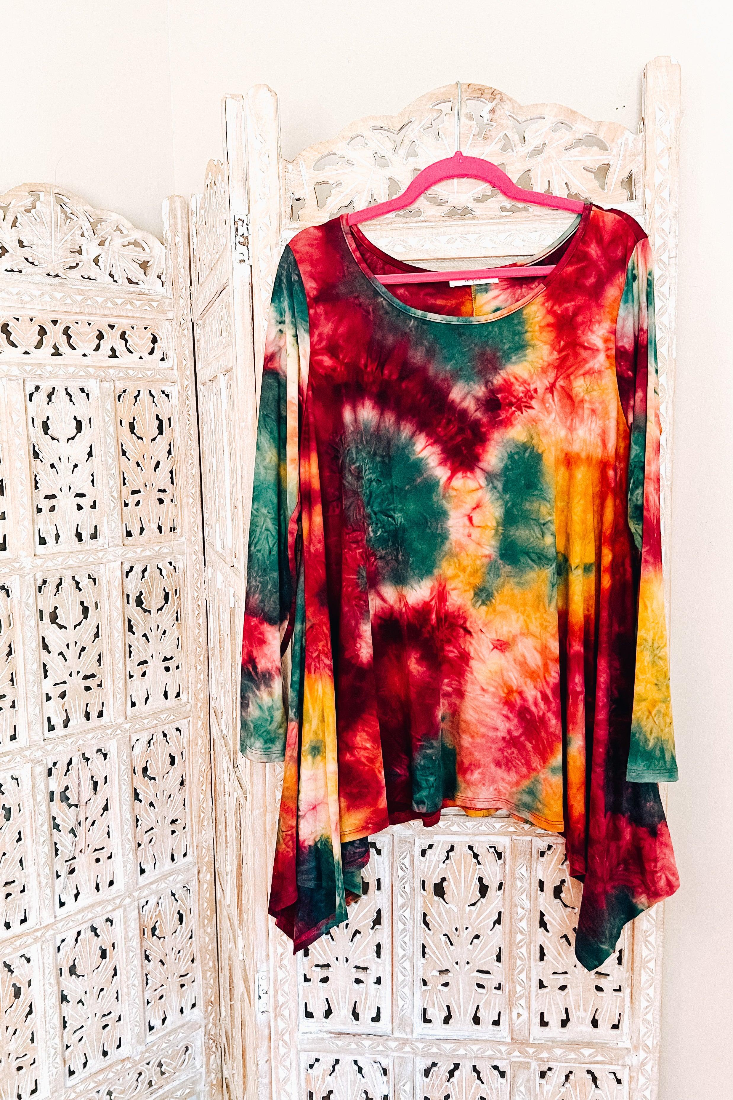 Long-sleeve tie-dye top in ruby, green, and mustard with an asymmetrical hem, hanging on a pink hanger