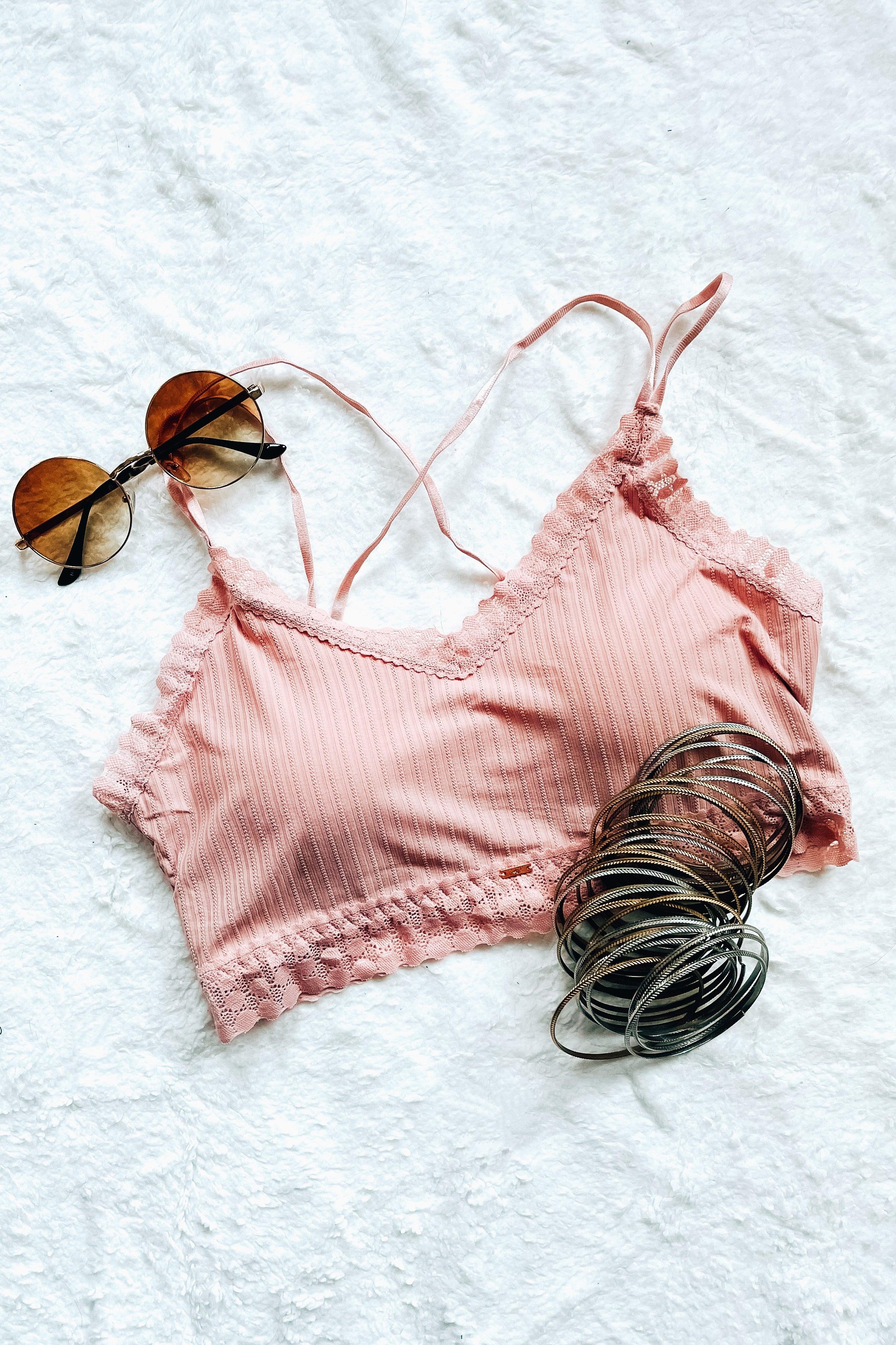 Pink lace bralette with ribbed texture and scalloped edges, styled with round sunglasses and metallic bangles on white background