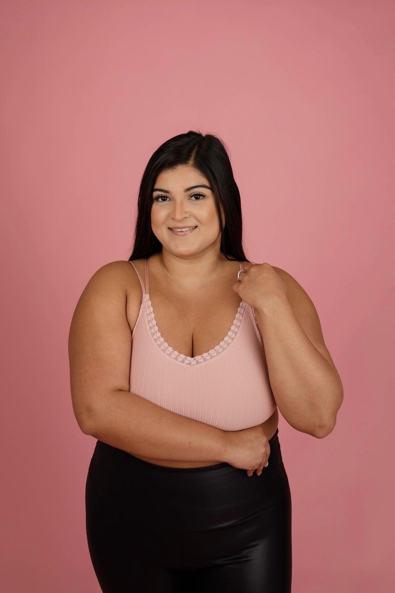 Woman wearing a pink ribbed bralette with lace edging and thin straps paired with black faux leather pants against a pink backdrop