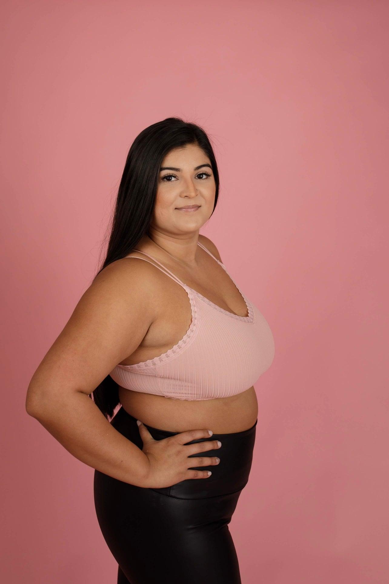 Curvy woman modeling soft pink ribbed lace bralette with double thin straps against solid pink background