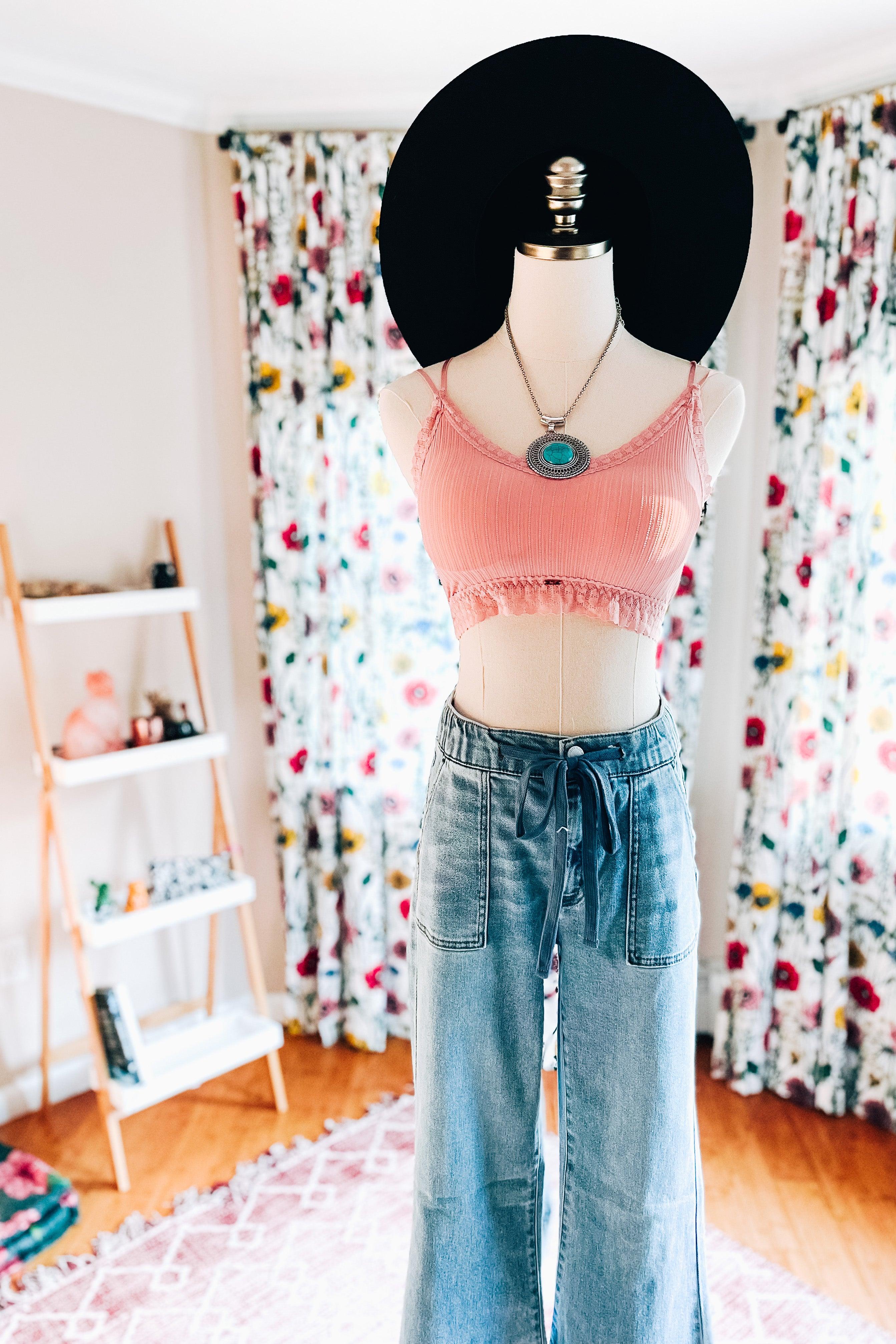 Pink ribbed bralette with lace trim on mannequin wearing wide-brimmed black hat and high-waisted blue jeans