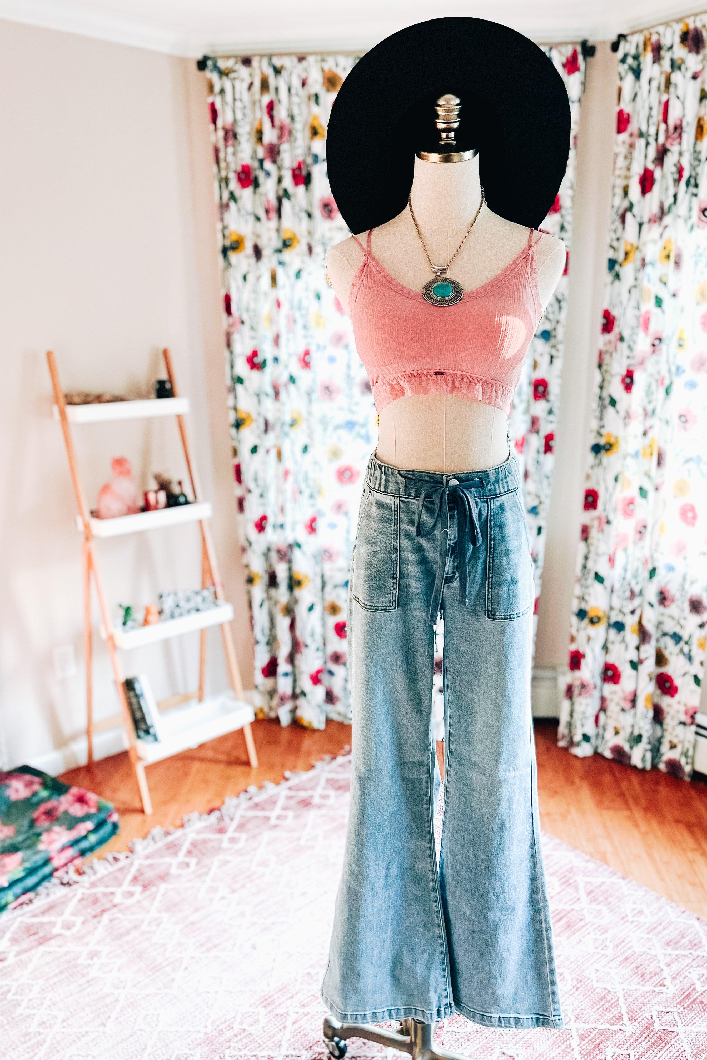 Pink ribbed crop top with lace trim paired with high-waisted blue wide-leg jeans on a mannequin wearing a black hat