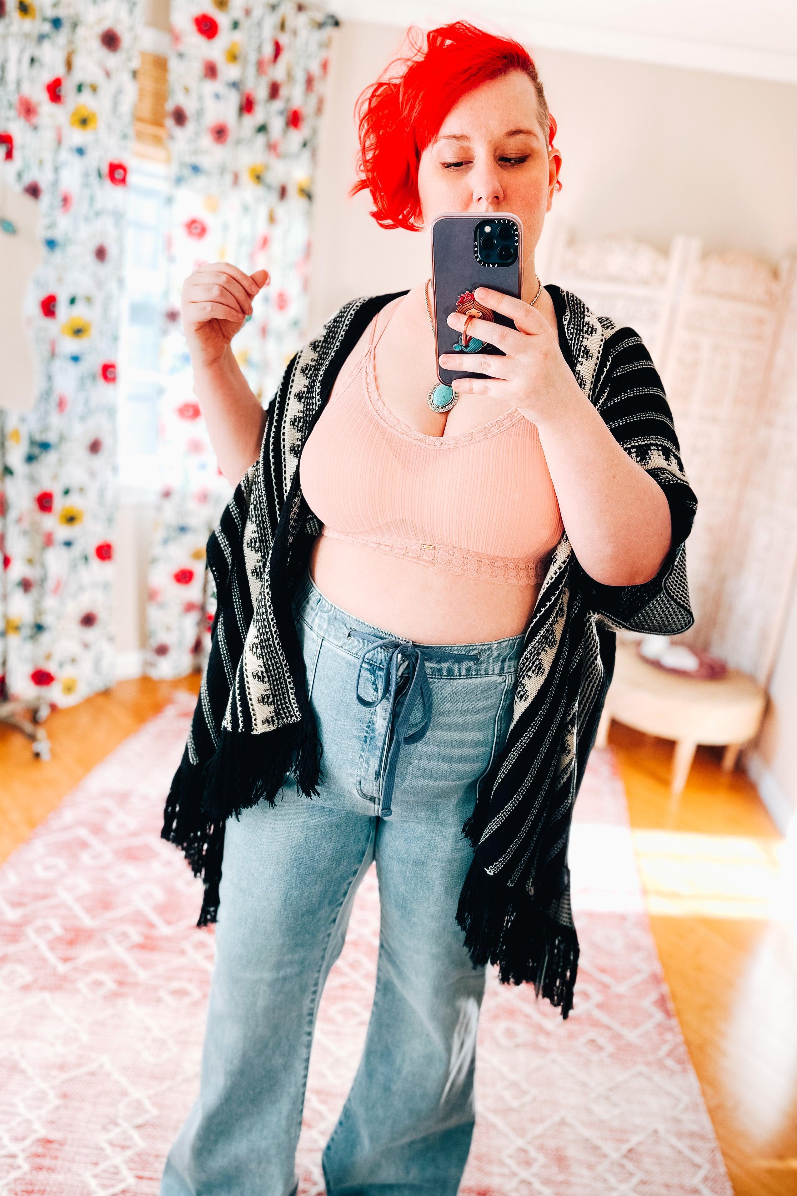 Woman wearing a soft pink lace-trimmed bralette paired with light blue drawstring jeans and a black patterned shawl