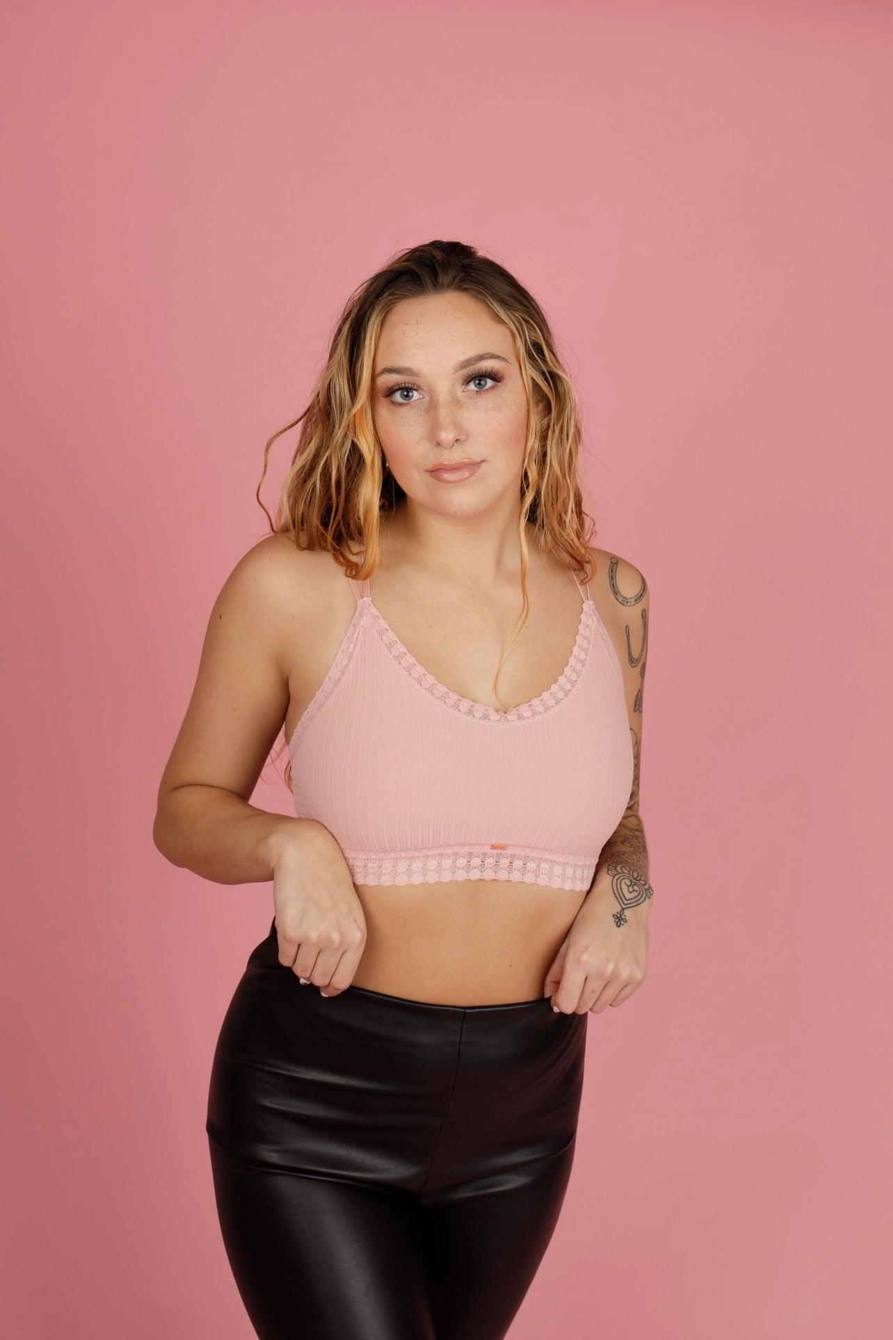 Woman wearing soft pink ribbed bralette with lace trim and black faux leather pants against pink background