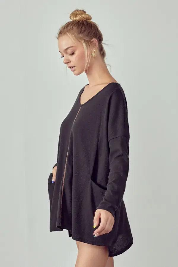 Woman wearing a loose black oversized thermal tunic with front pockets and a subtle center seam detail