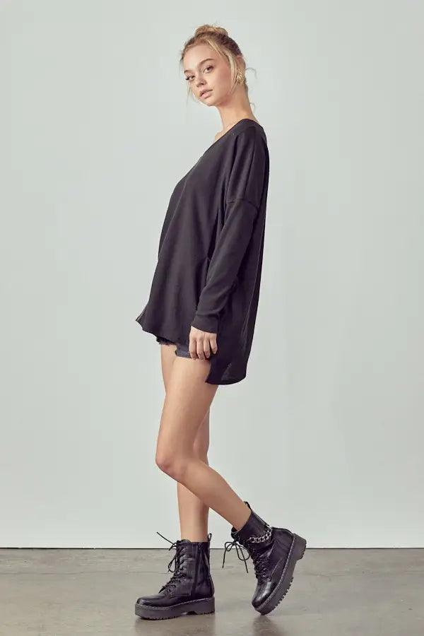 Young woman wearing loose black thermal tunic styled with black shorts and lace-up combat boots against plain background