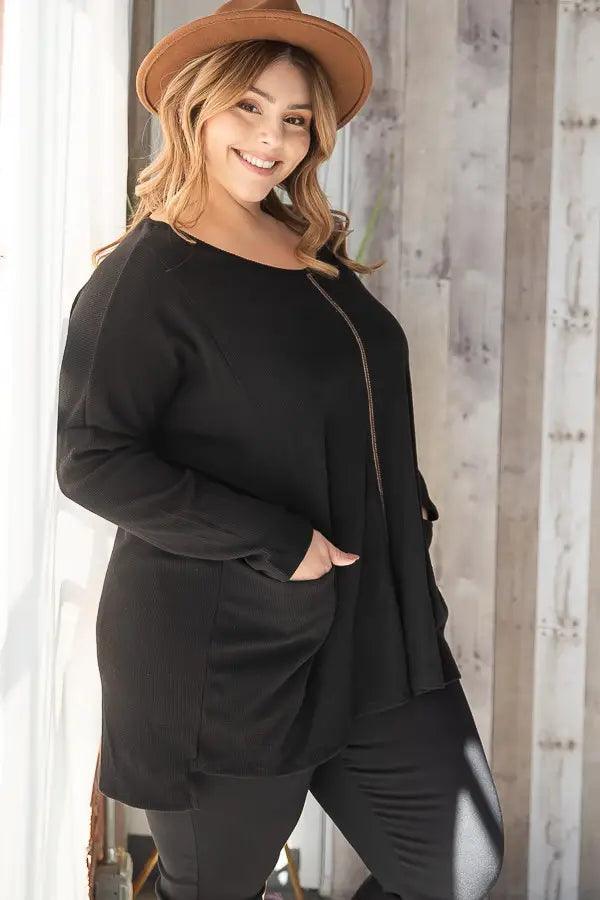 Smiling woman wearing a relaxed black oversized thermal tunic with subtle seam detail and front pockets indoors