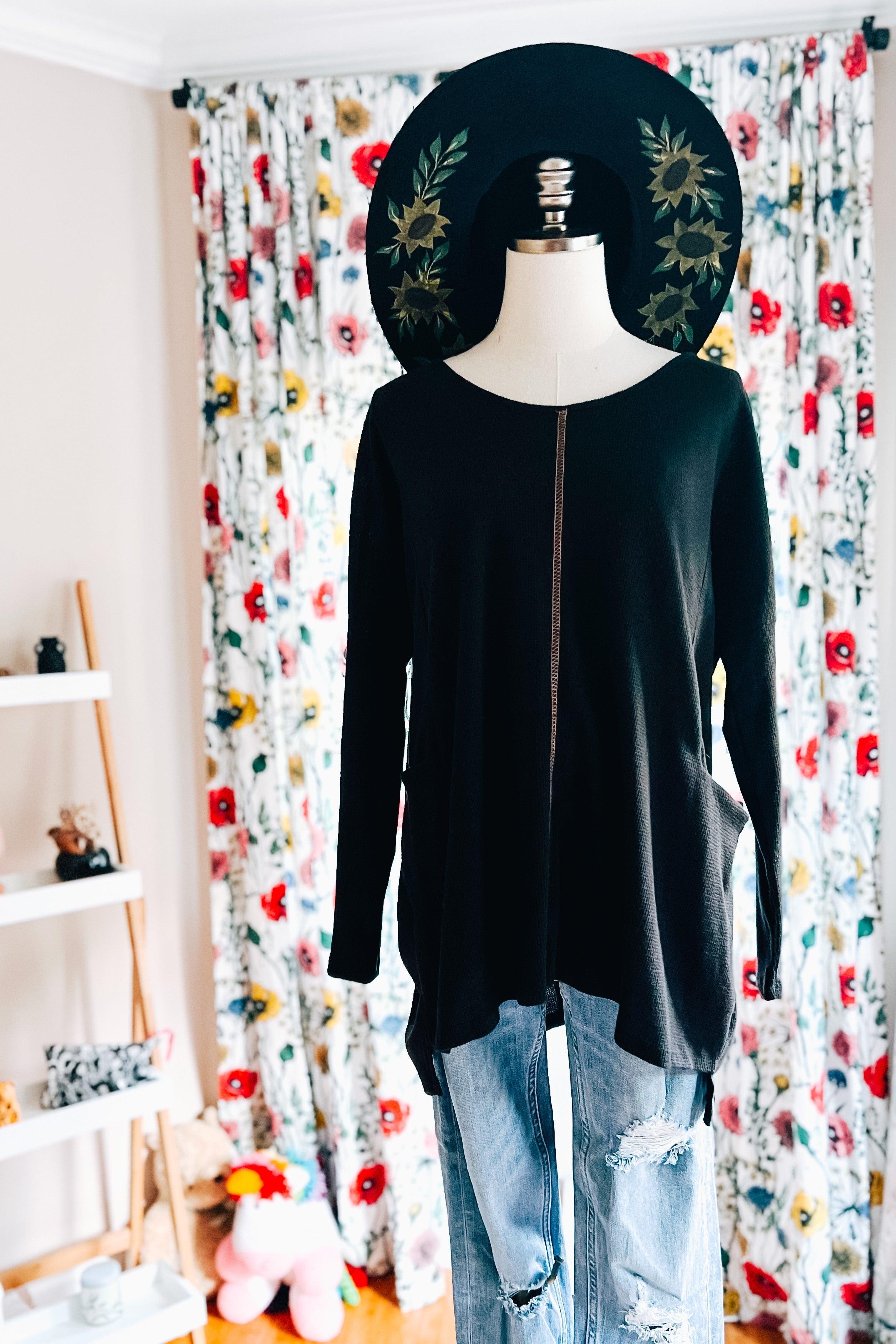 Black oversized tunic with front seam detail styled on mannequin wearing distressed light blue jeans and floral hat