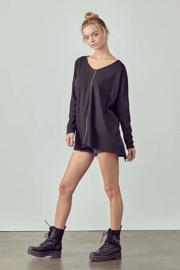 Model wearing a loose black long-sleeve tunic with a front seam paired with black shorts and lace-up boots