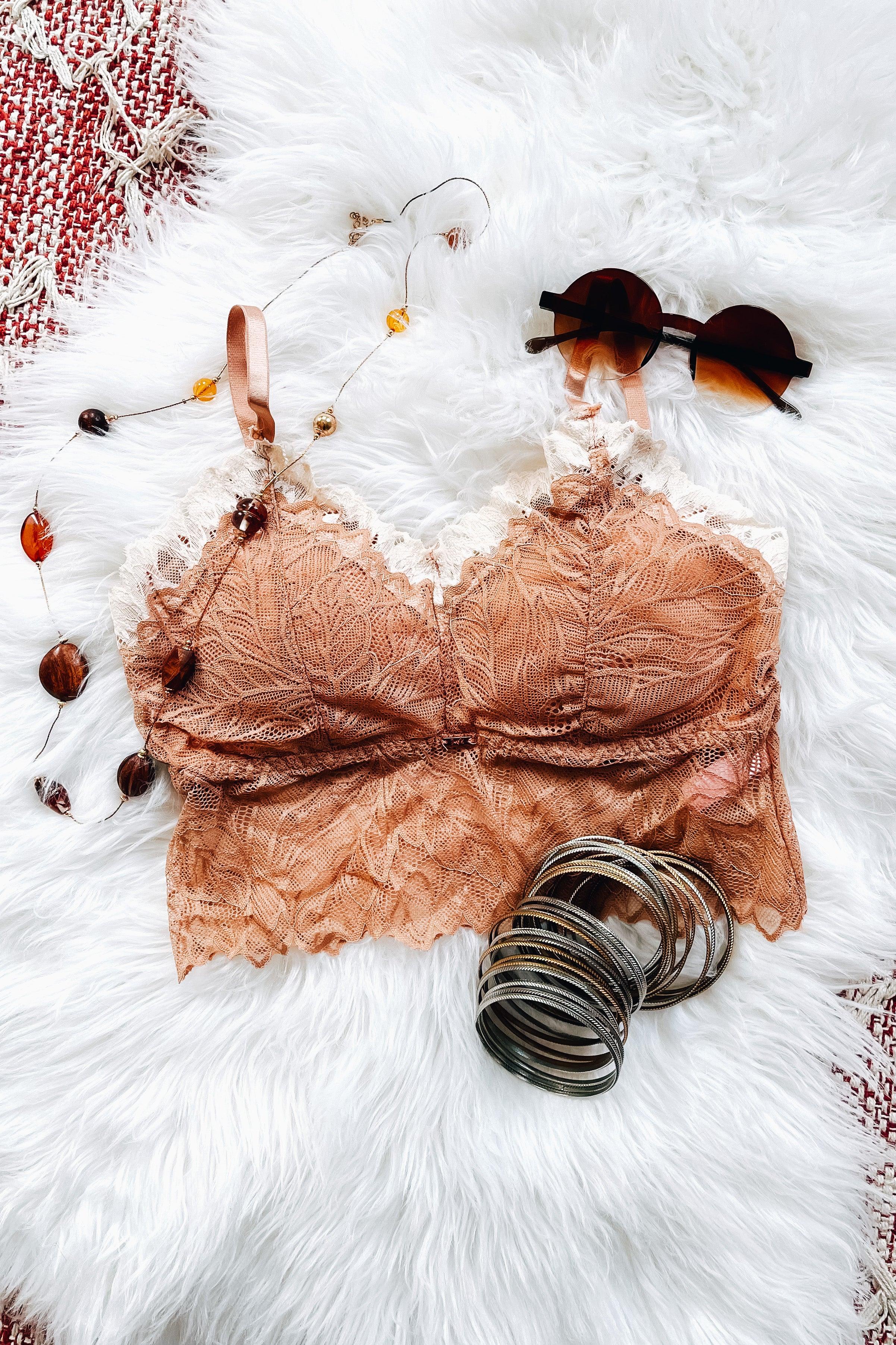 Delicate brick-colored lace bralette with scalloped edges, styled alongside round sunglasses and metallic bangles on a soft white surface.