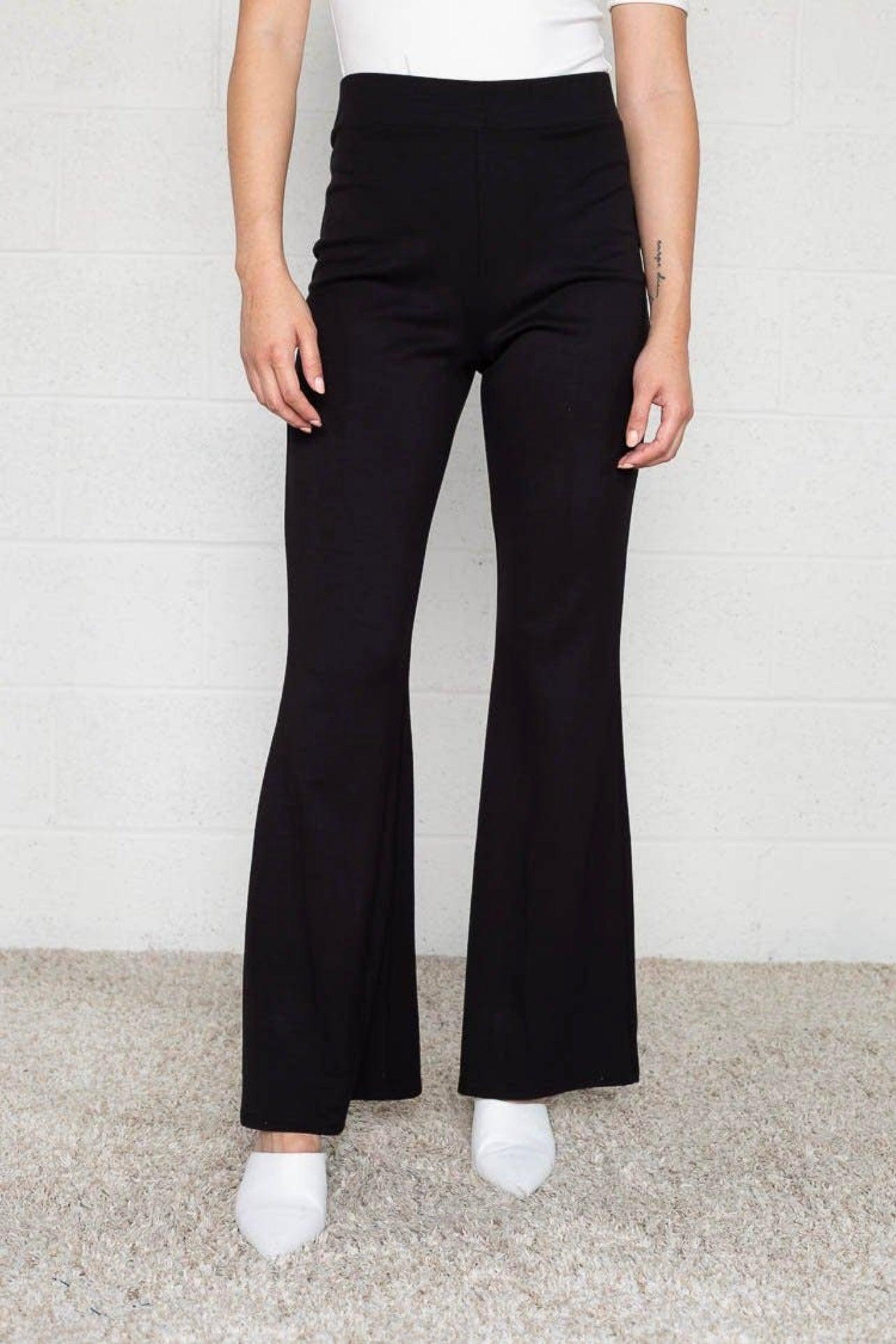 Black high-waisted flared pants styled with white pointed-toe shoes on neutral textured background