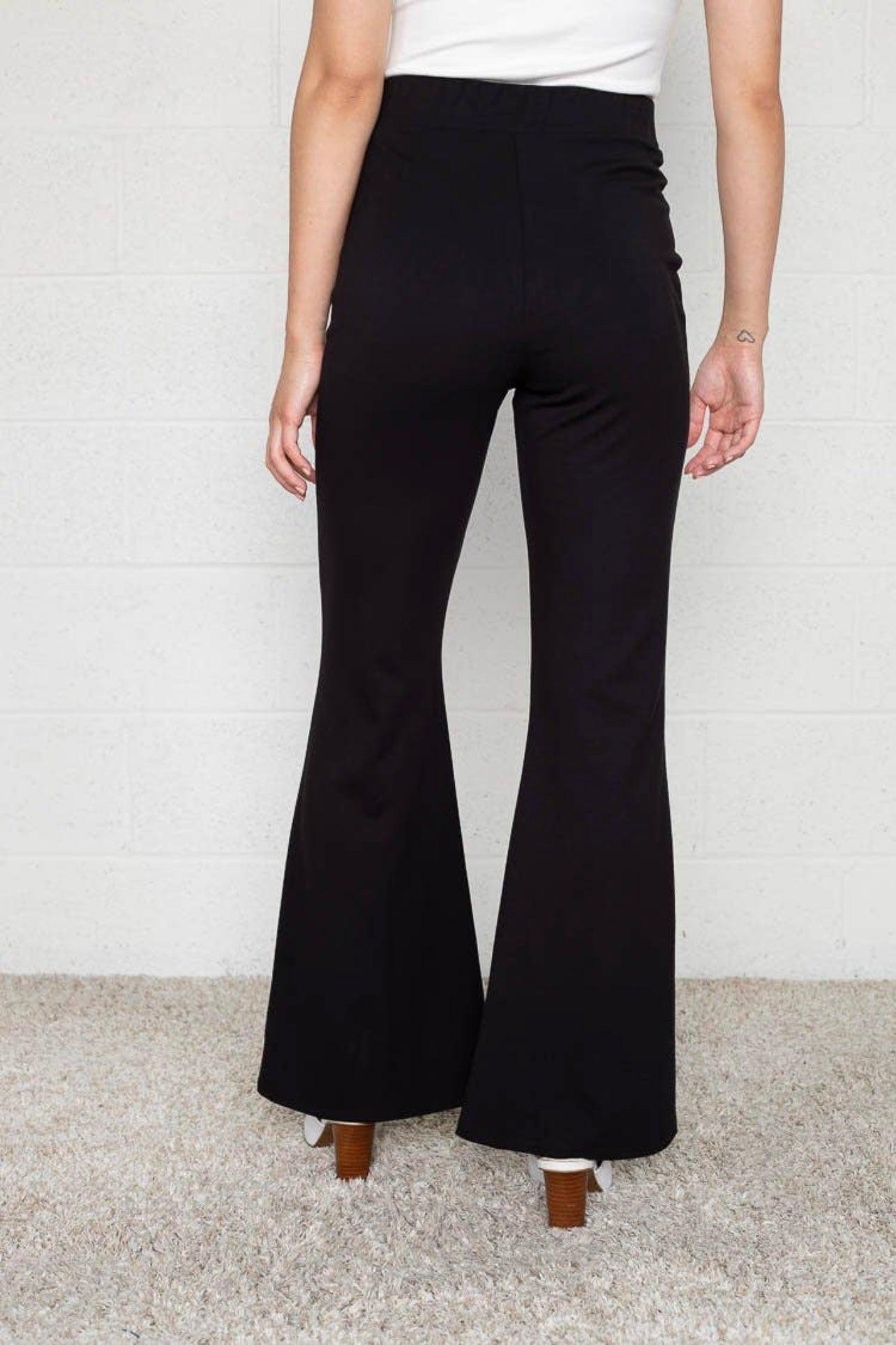 Rear view of black high-waisted flared pants paired with white top and brown heeled shoes on carpeted floor