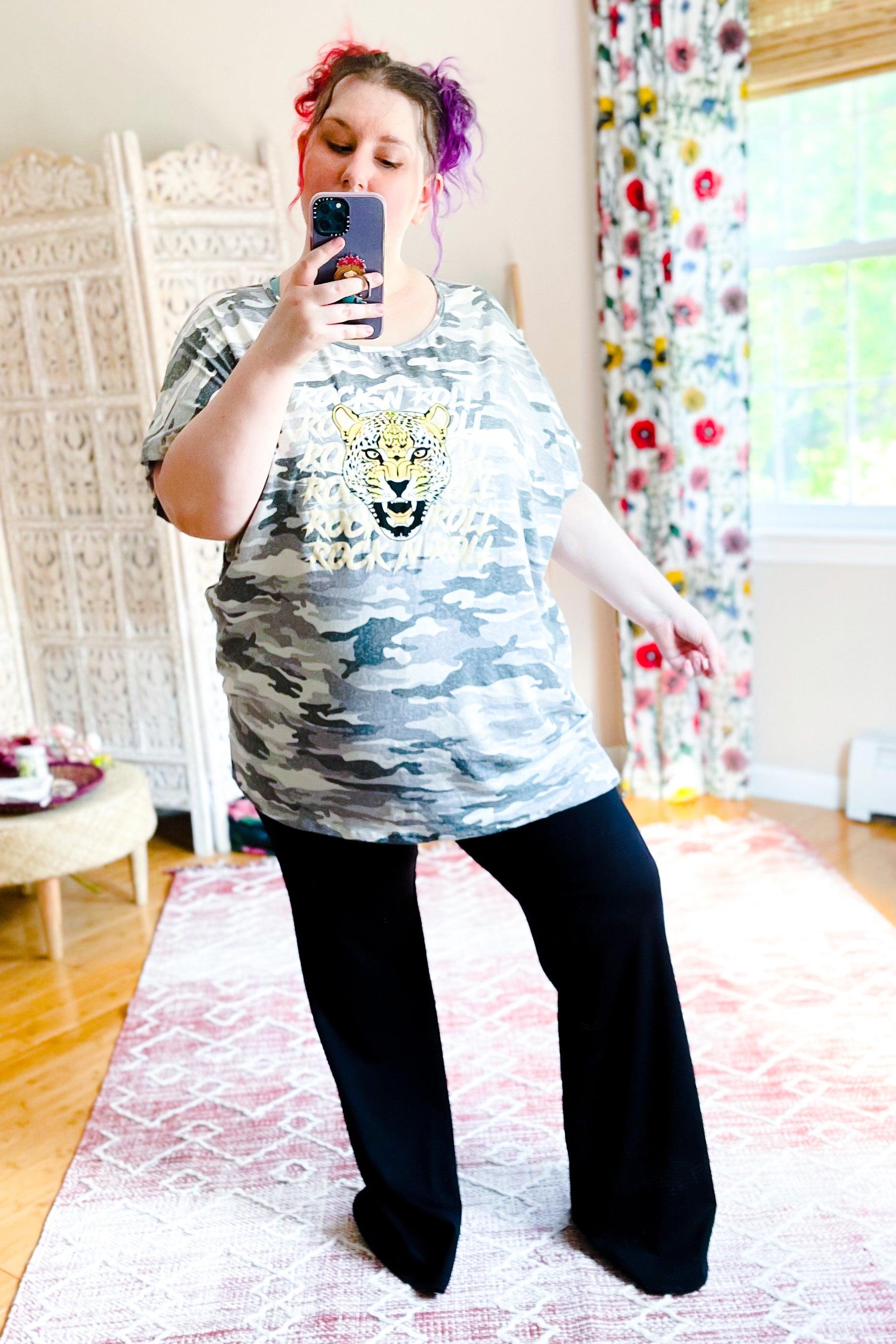 Woman with pink and purple hair wearing camouflage top and black wide leg Oh Baby Black Flares posing for mirror selfie in bright room