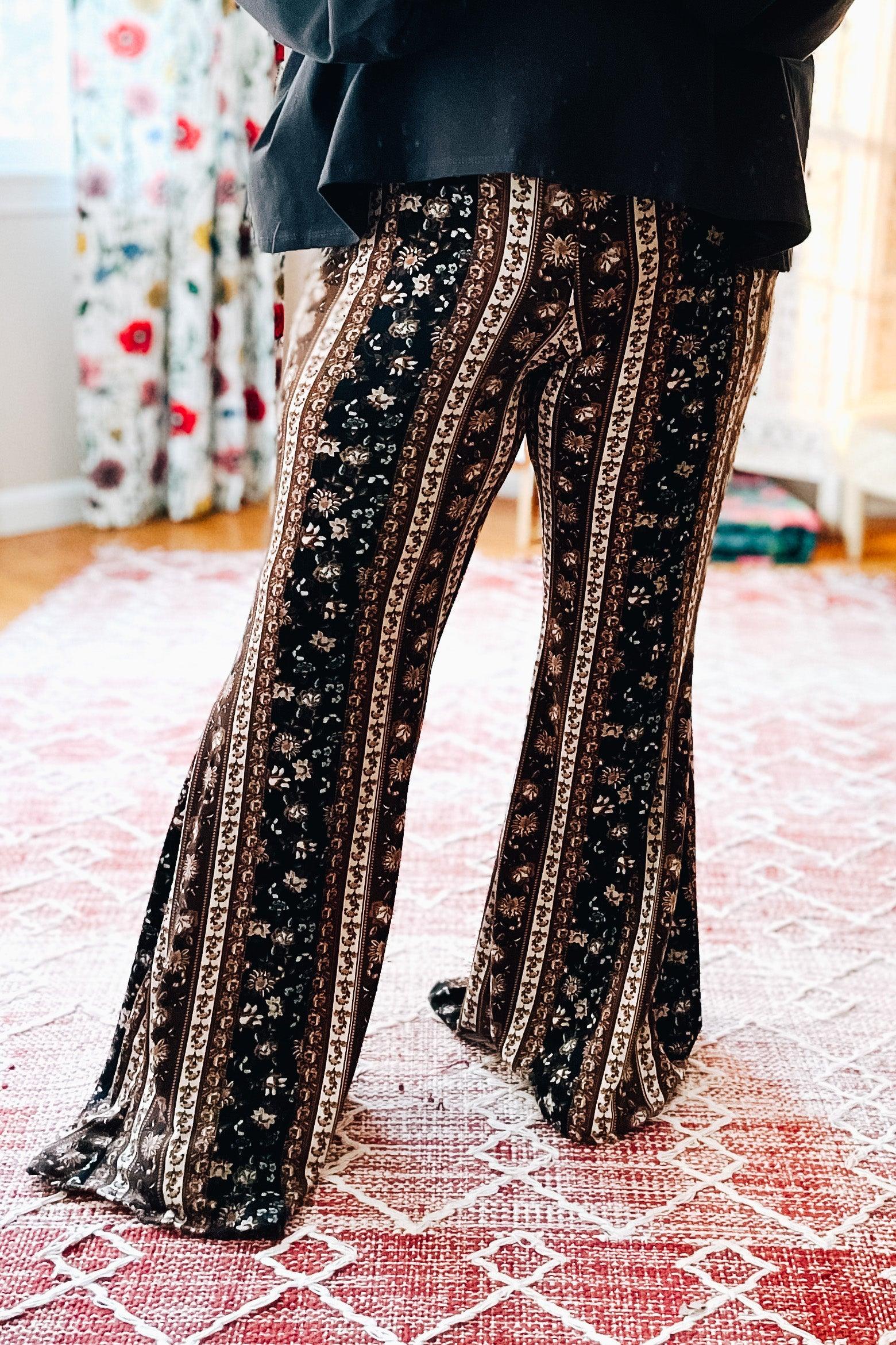 Woman wearing navy and brown paisley patterned bell bottoms with a relaxed black top standing indoors on patterned rug